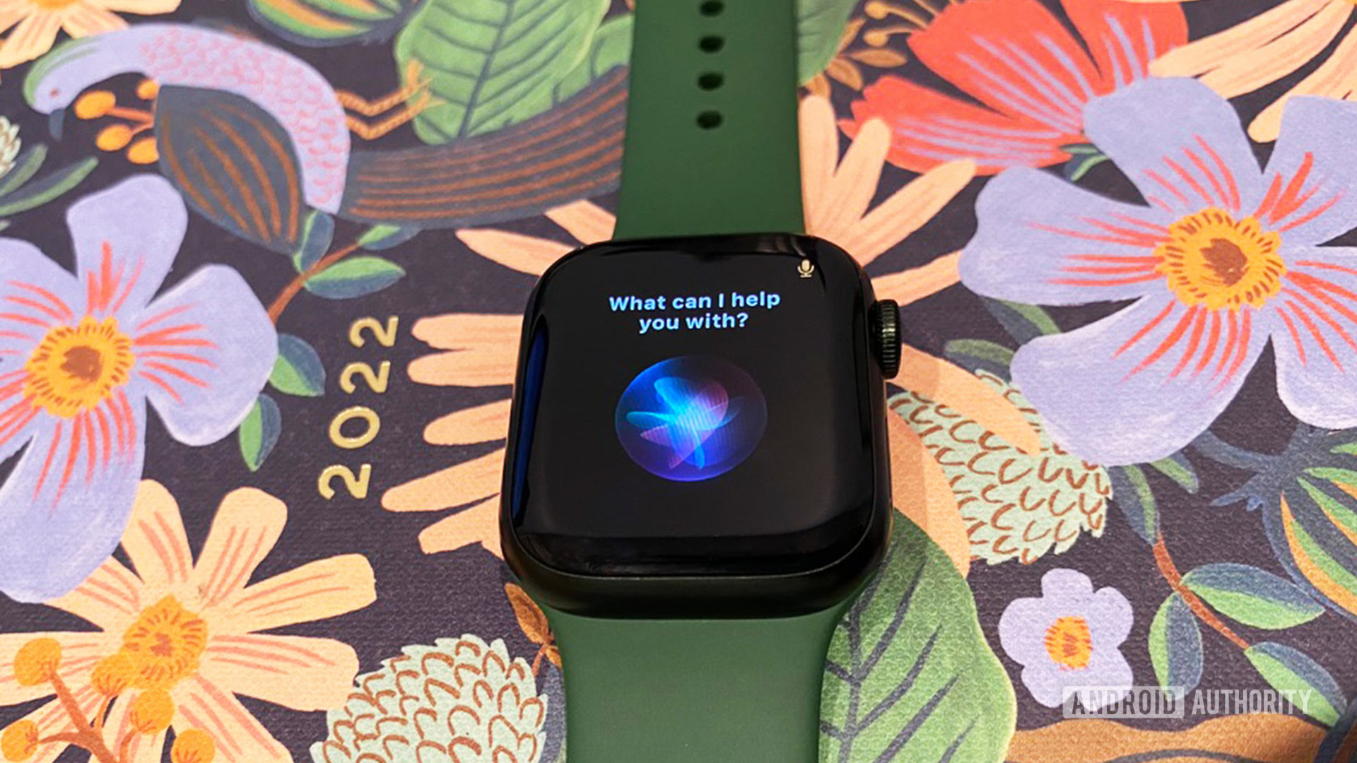 An Apple Watch Series 7 rests on a floral planner with Siri activated on screen.