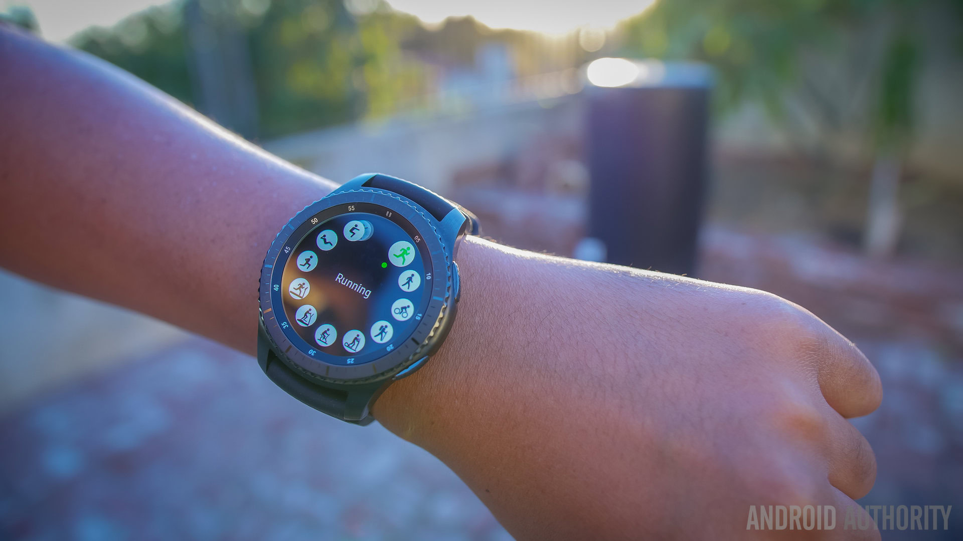 The Samsung Gear S3 smartwatch on a wrist in a park at sunset. 