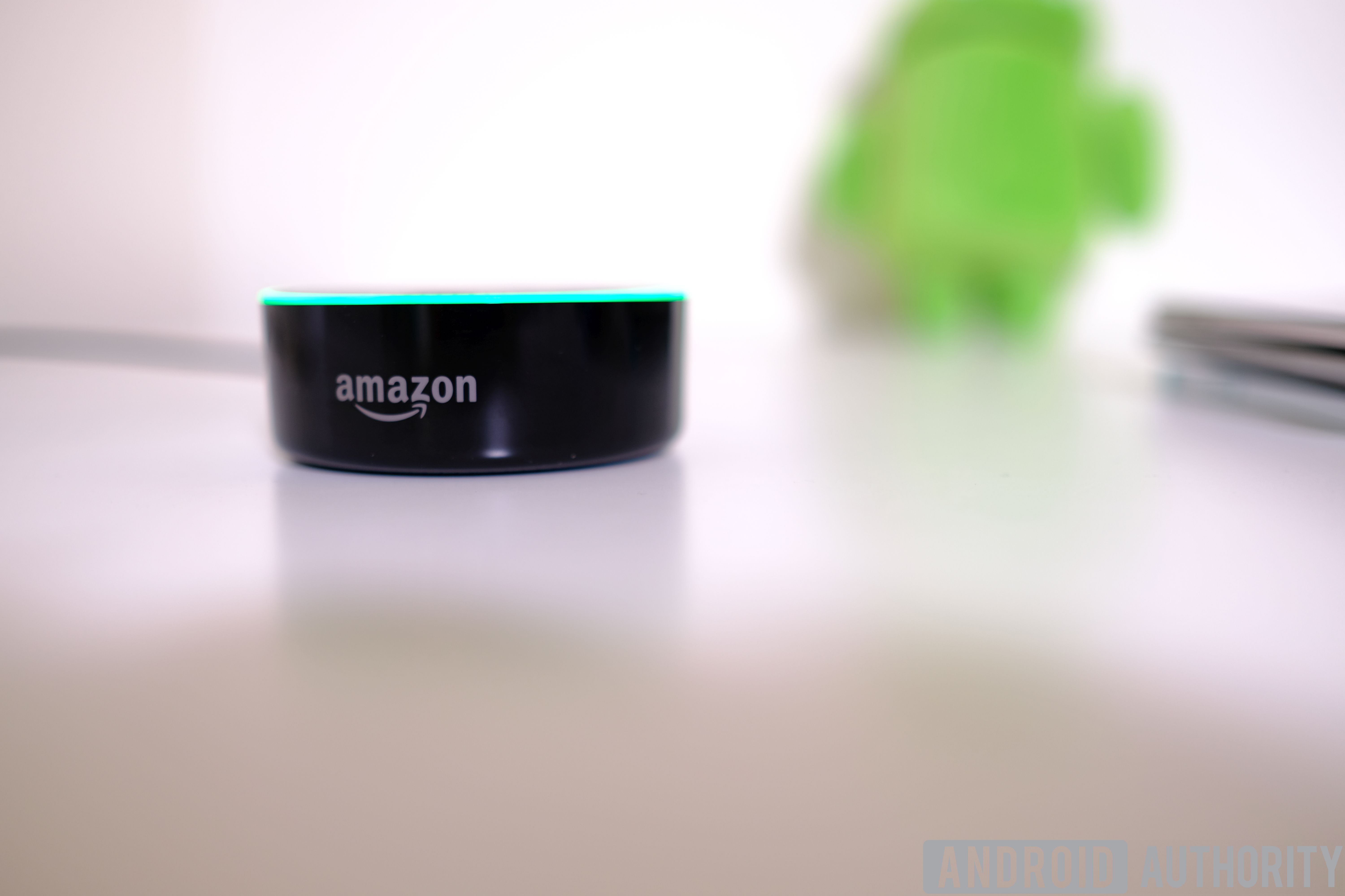 Amazon Echo Dot image on white surface with Android figurine in background.