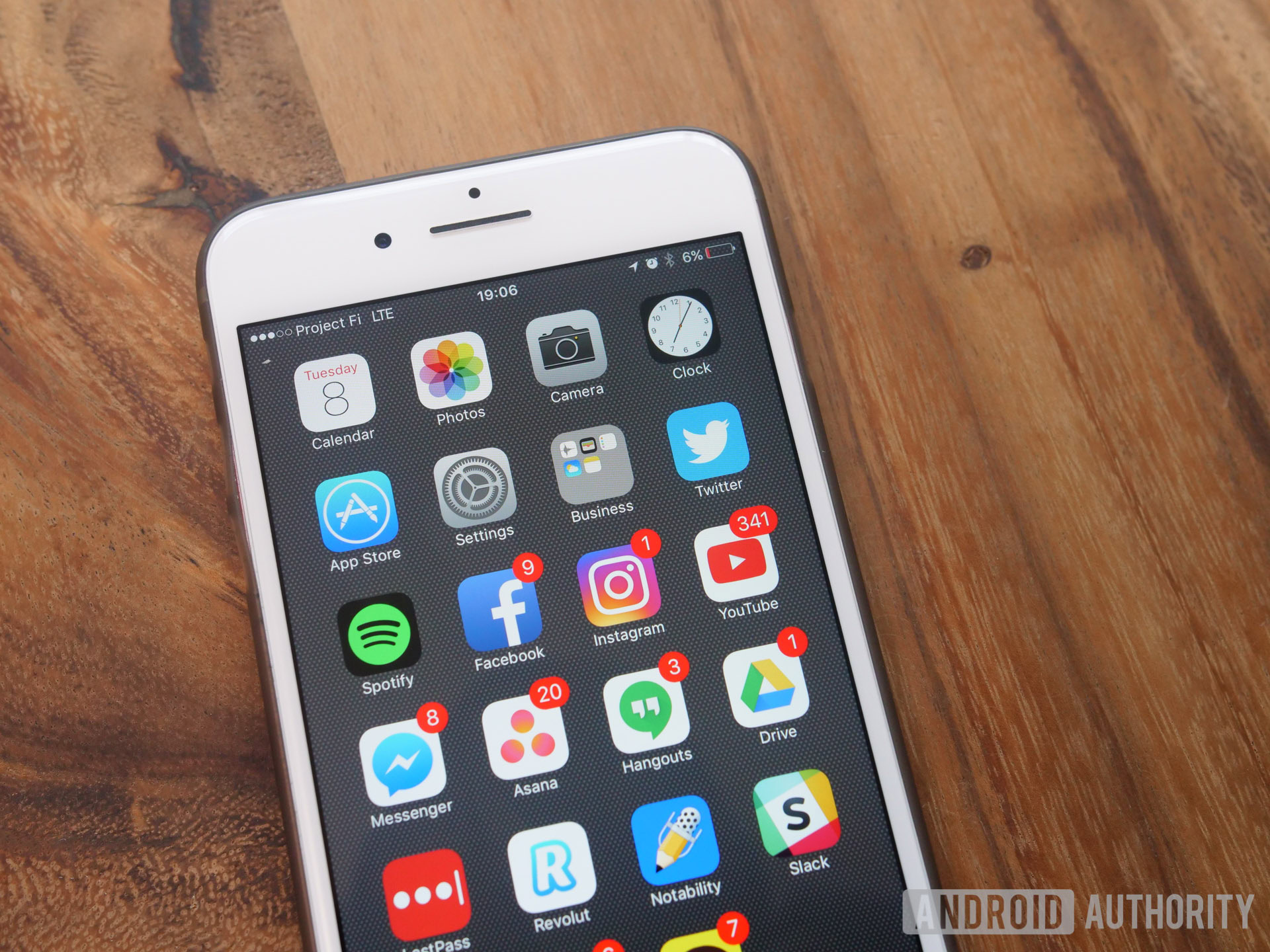 A photo of a white iPhone 7 resting on a wood surface showing its touchscreen.