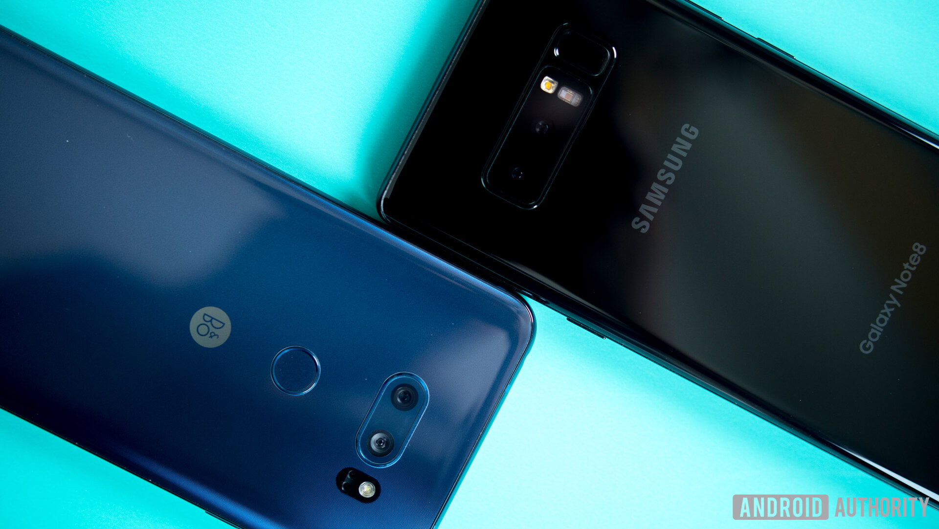 The LG V30 and Galaxy Note 8 smartphones, face-down on a turquoise surface.