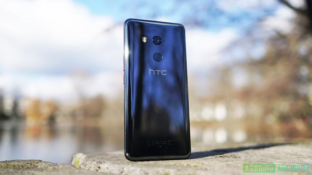 The HTCU11 Plus smartphone on a stone in front of a lake on a sunny day.