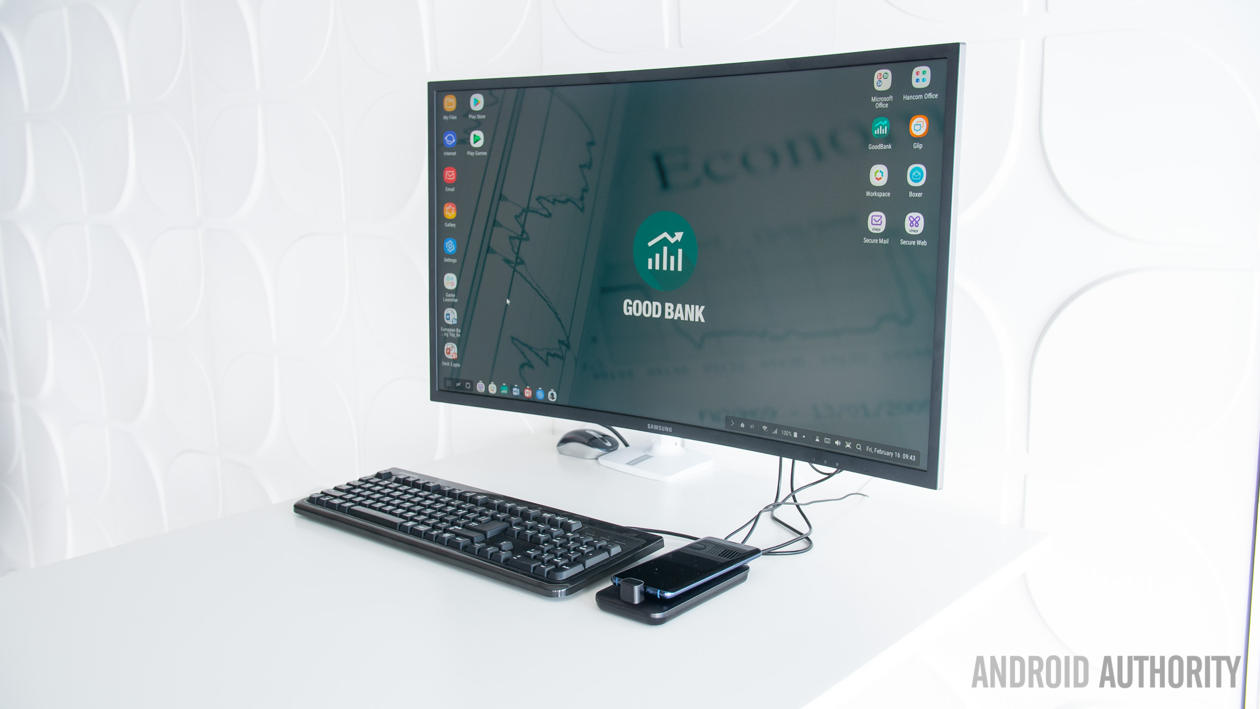 The Samsung Dex Pad on a white desk with a monitor and keyboard next to it.