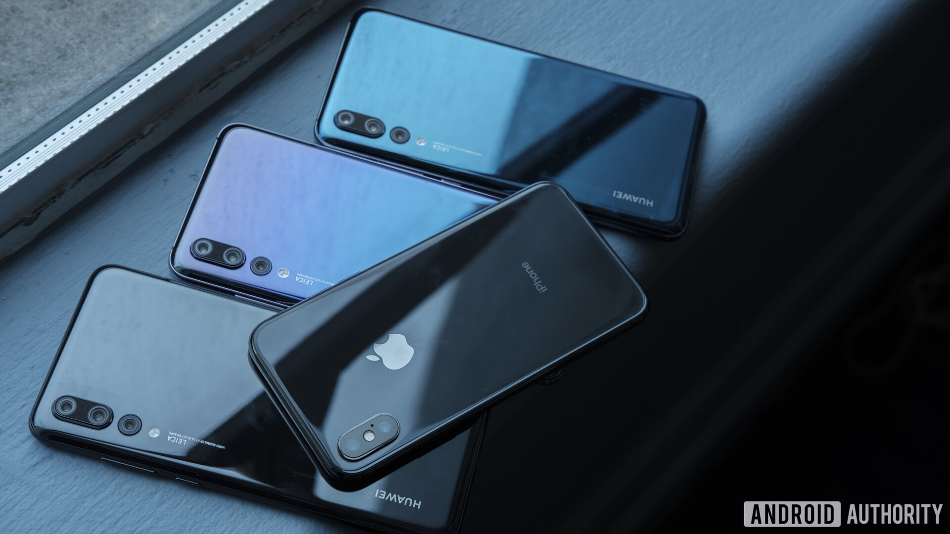 The Apple iPhone X on top of three HUAWEI P20 Pro smartphones on a window ledge.