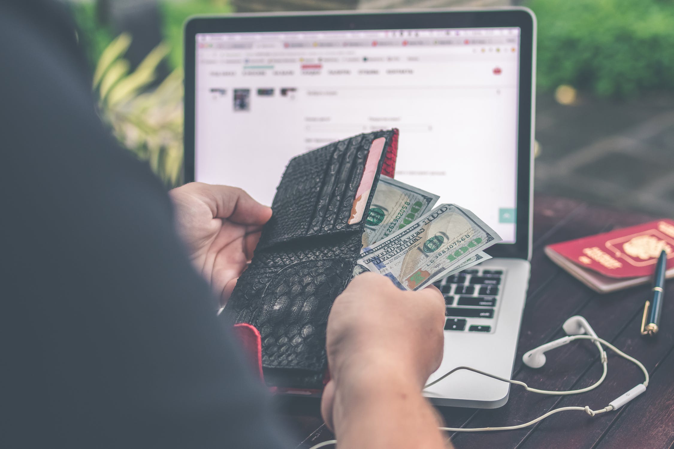 picture of man taking cash out of his wallet while in front of laptop