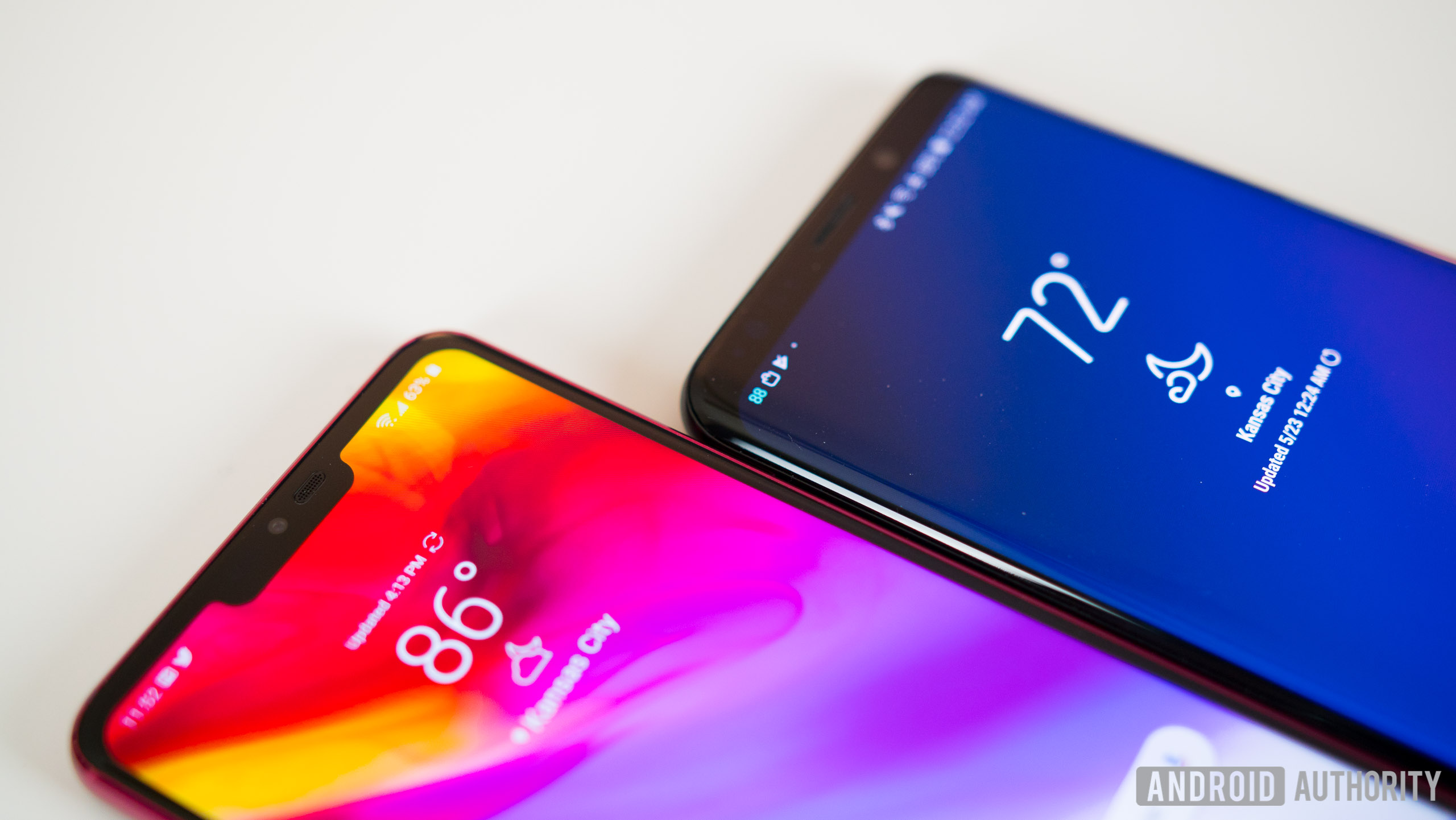 The LG G7 ThinQ and Samsung Galaxy S9 Plus, face-up on a white desk next to each other.