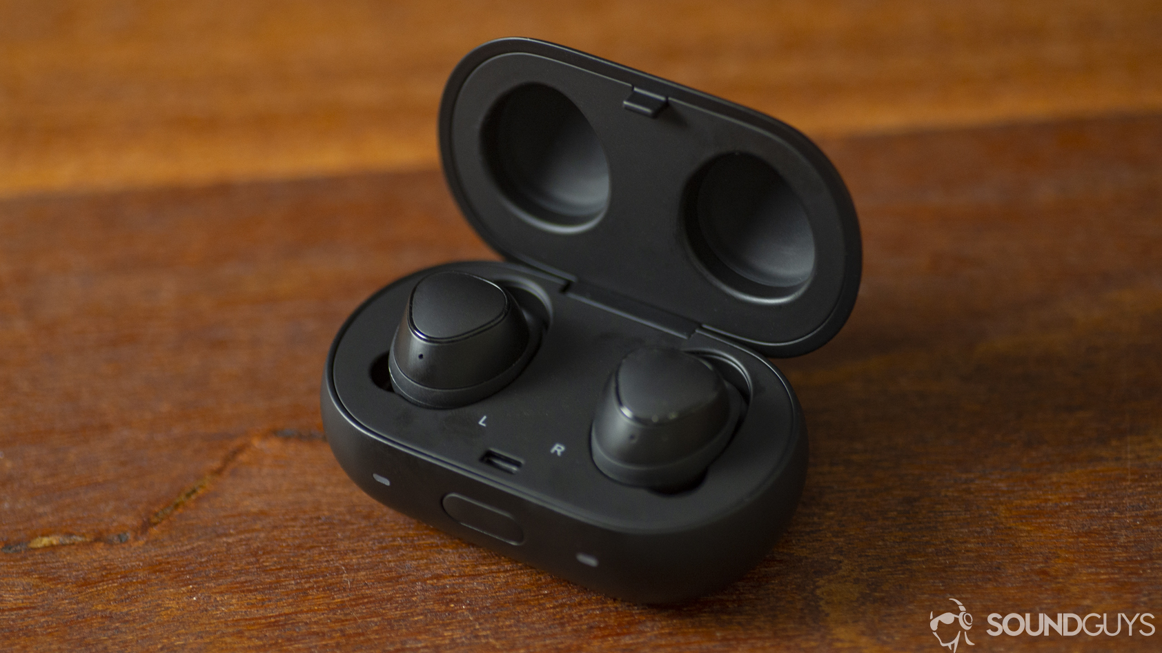 A photo of the Samsung Gear IconX with charging case on a wood desk.