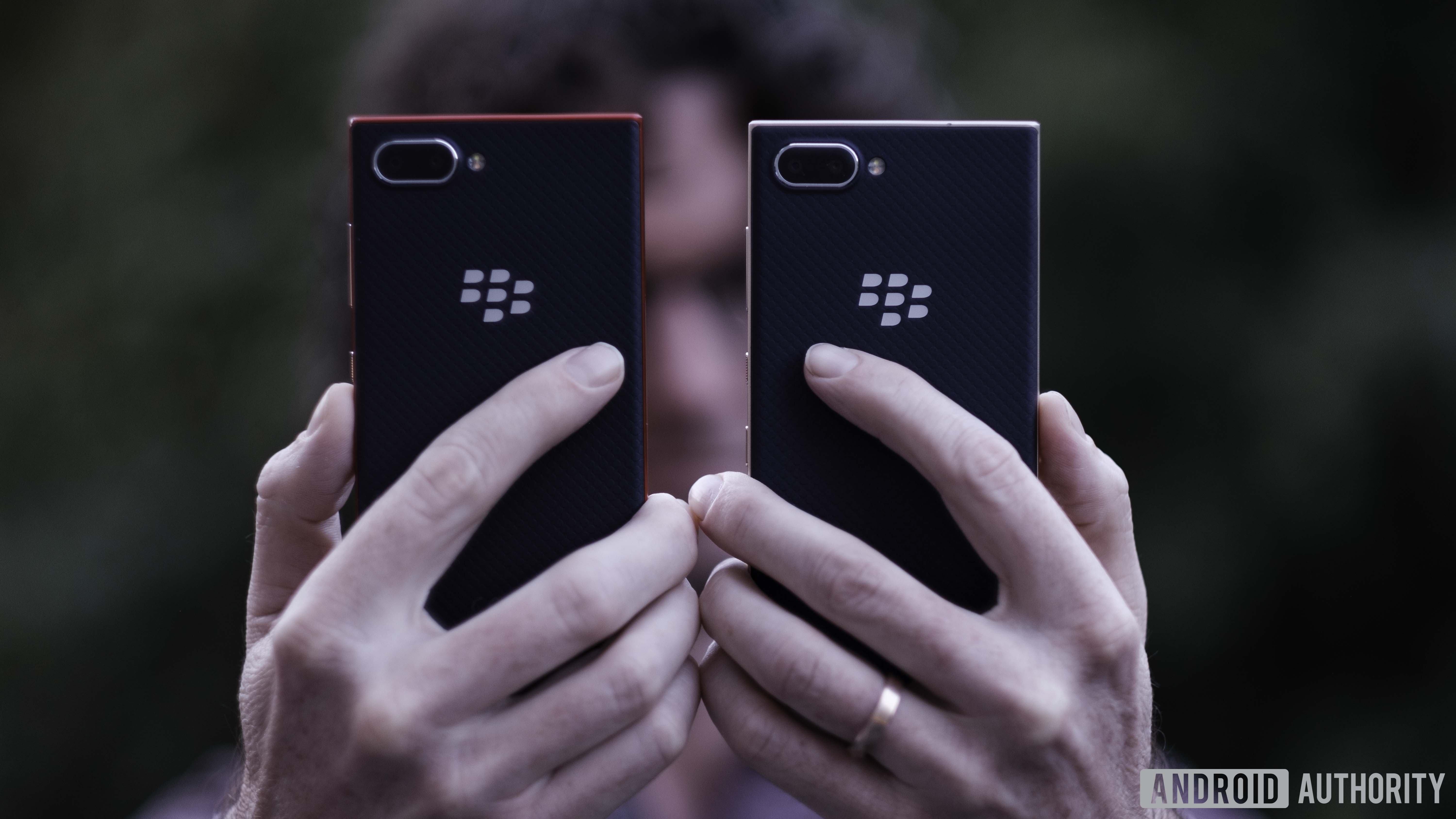 Holding two Blackberry Key2 LE devices showing backs, cameras, and BlackBerry logo