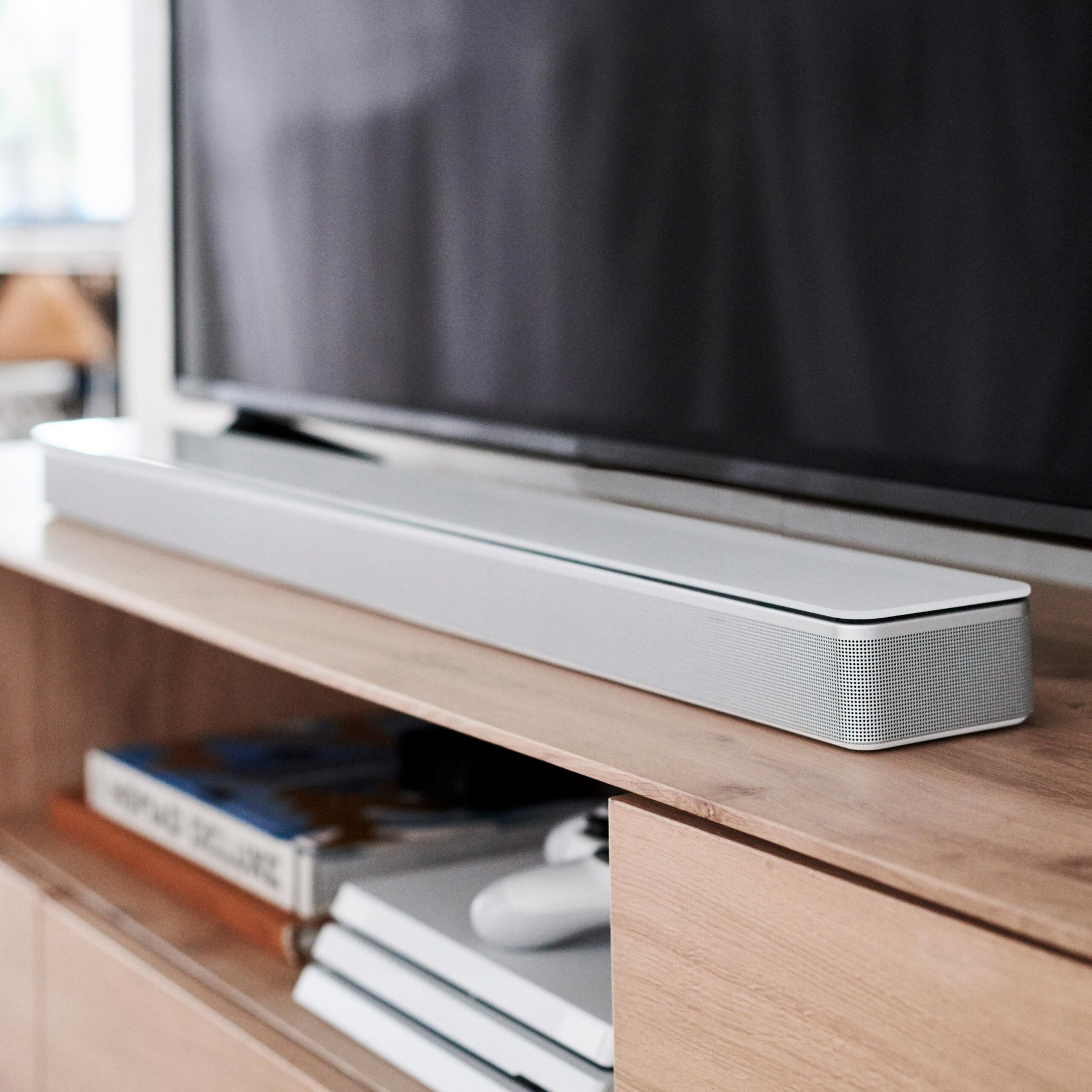 Bose smart speaker soundbars: Product image of the Bose Souundbar 700 (white) from Bose press release. The soundbar sits ona wood TV stand with a TV above it.