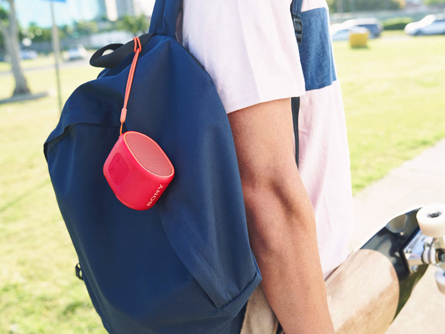 Sony SRS-XB01 image from embargo. The red compact speaker is attached to a man's navy backpack.