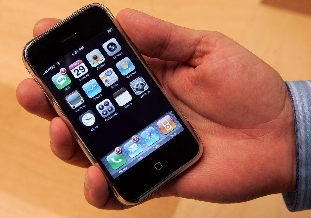 A picture of a hand holding the original Apple iPhone.