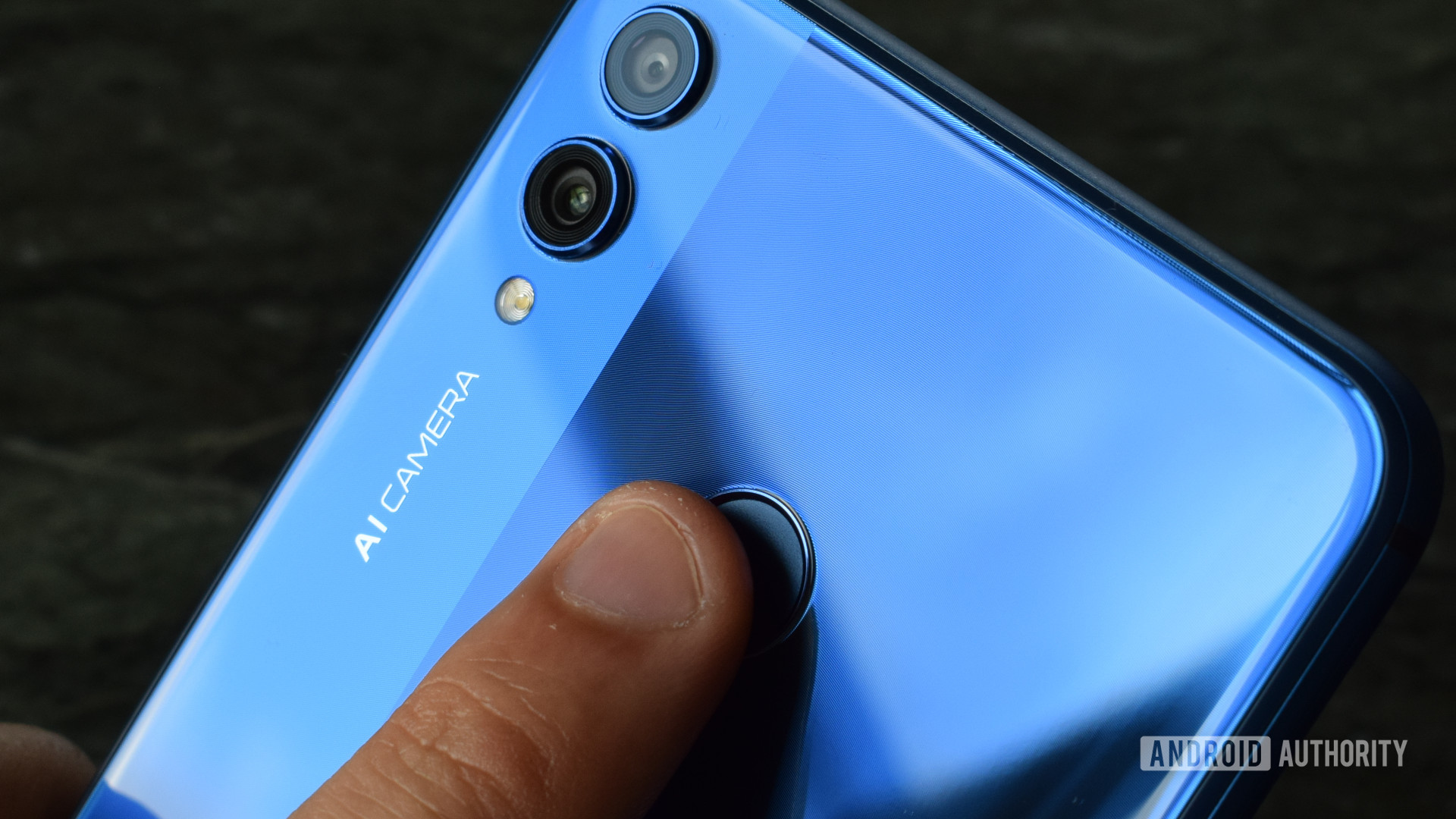 A finger against a blue smartphone's fingerprint sensor. 