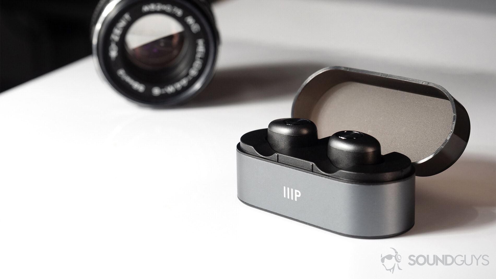 Monoprice cheap true wireless earbuds in case an din front of a black vintage lens.