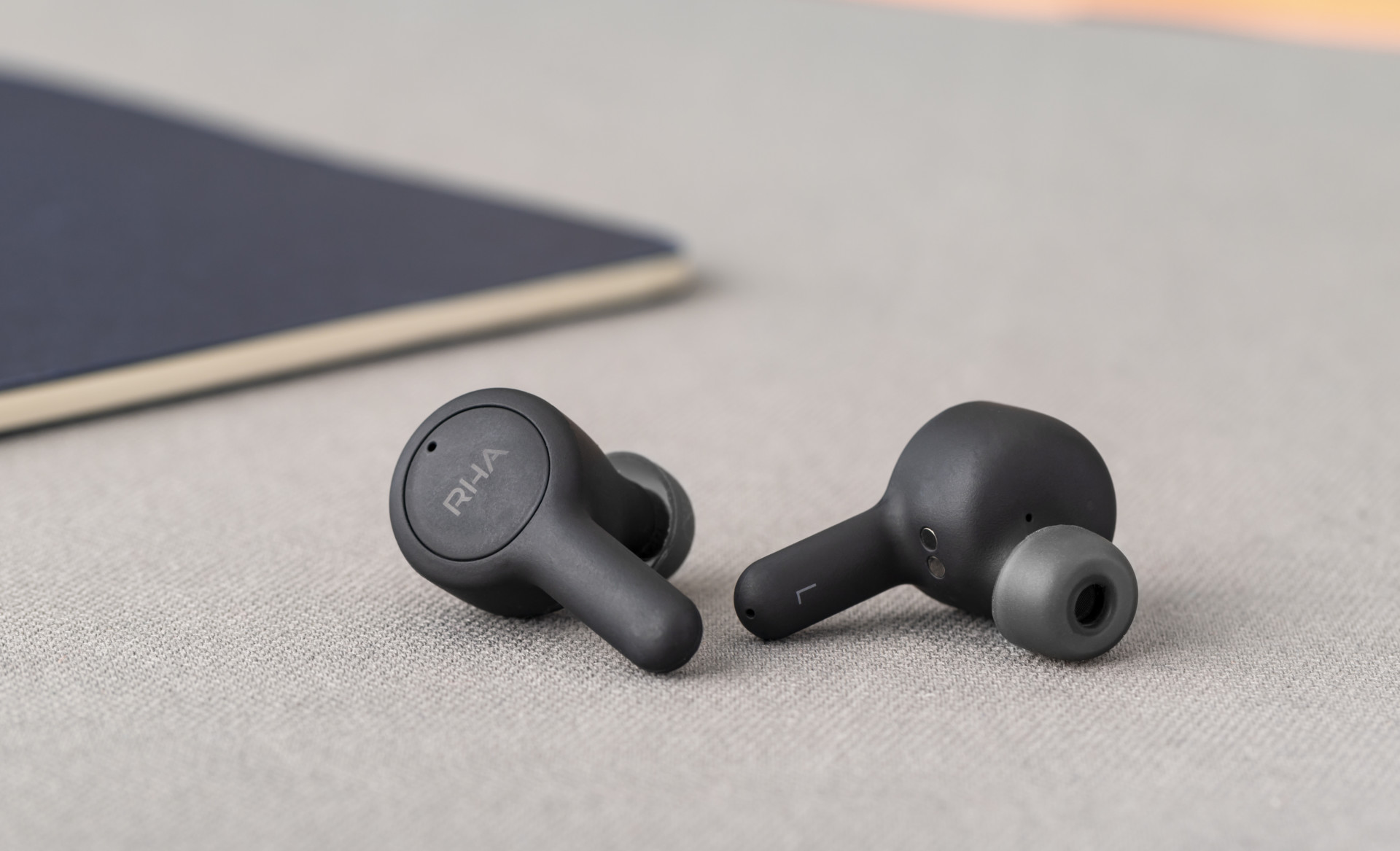 RHA TrueConnect: The earbuds on a beige surface.