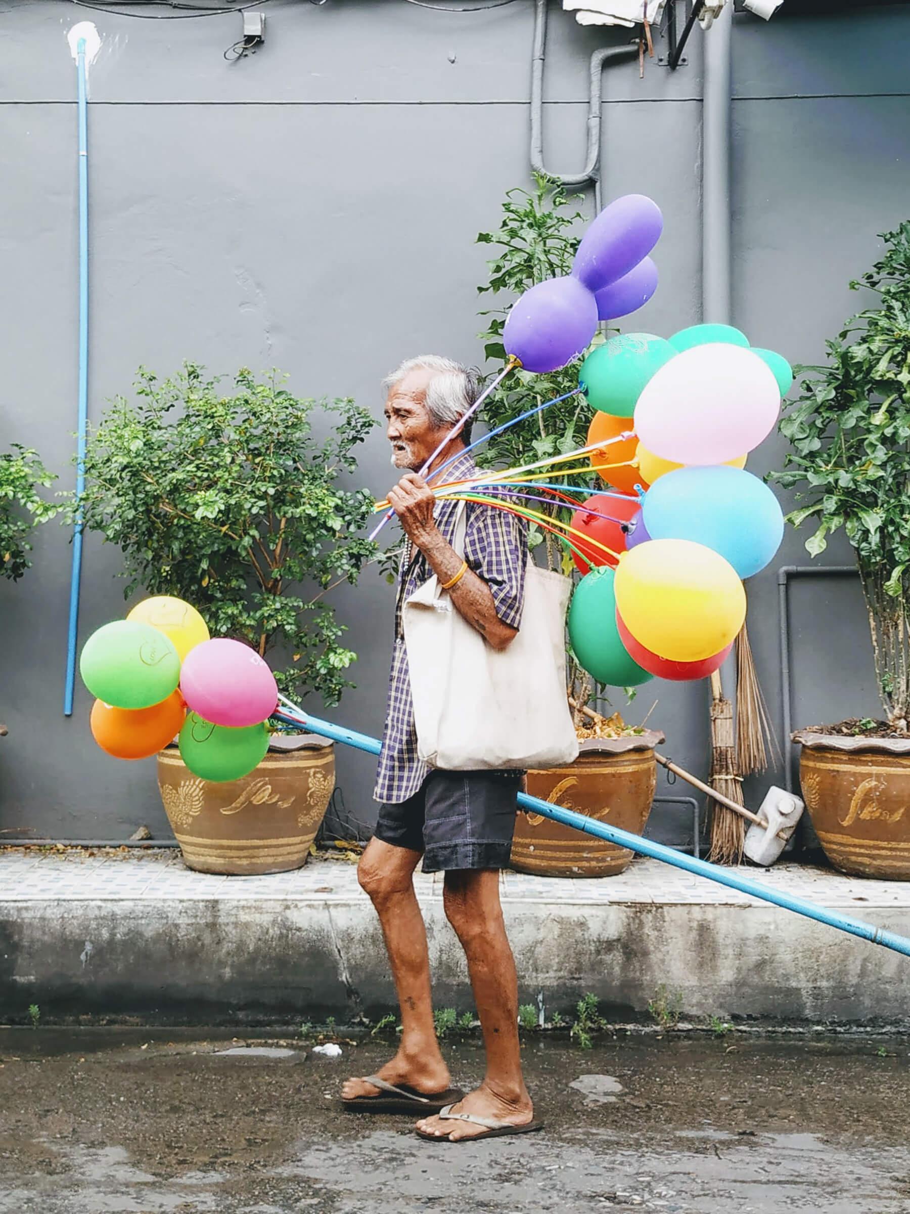 A photo of an old man carrying balloons.