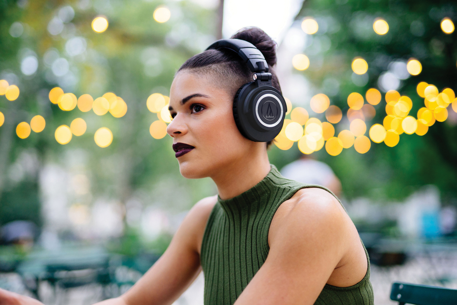 Audio-Technica ATH-M50xBT lifestyle image of headphones worn by woman sitting outdoors.