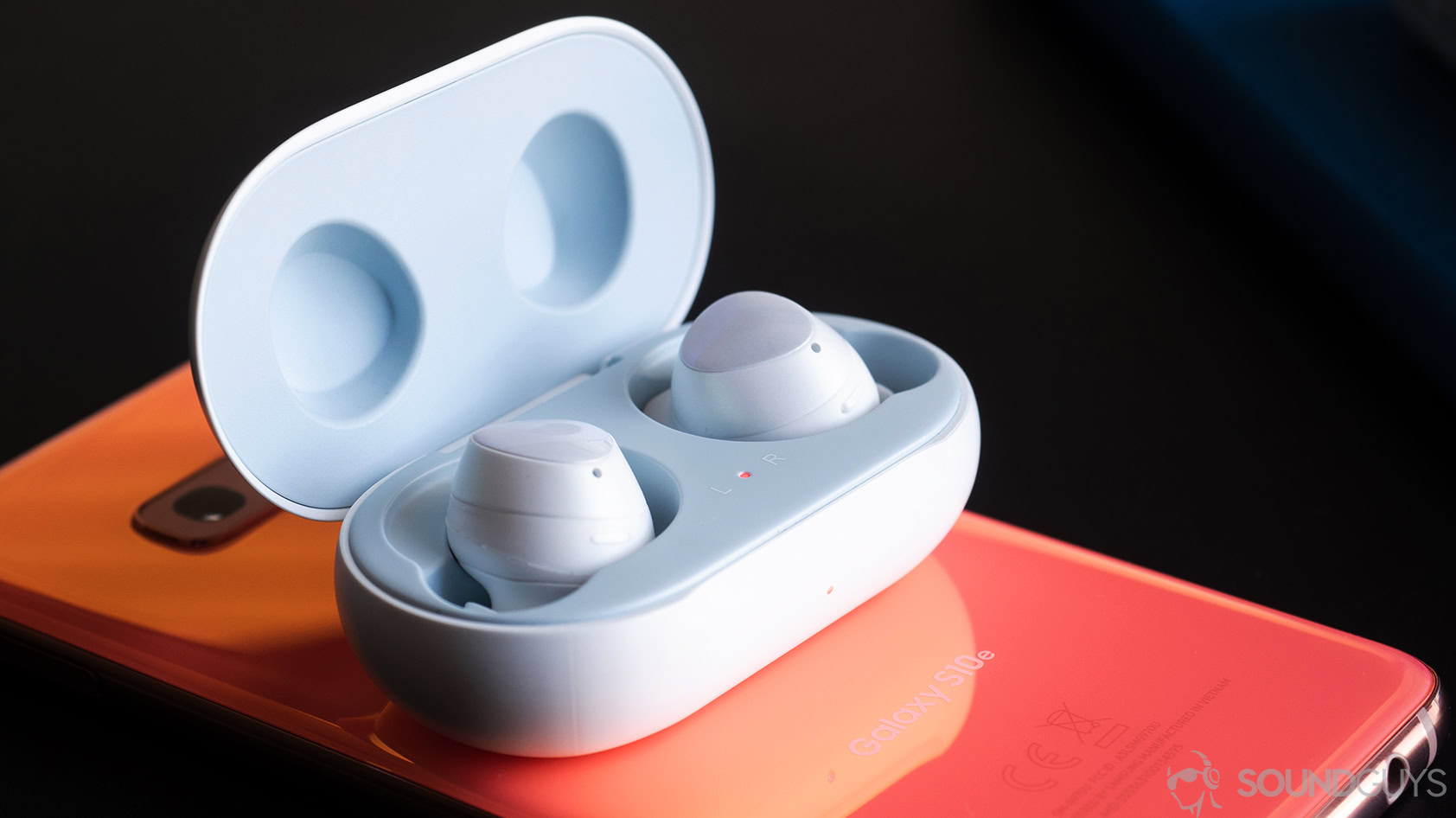 Samsung Galaxy Buds in case on top of a Samsung Galaxy S10e smartphone in Flamingo Pink.