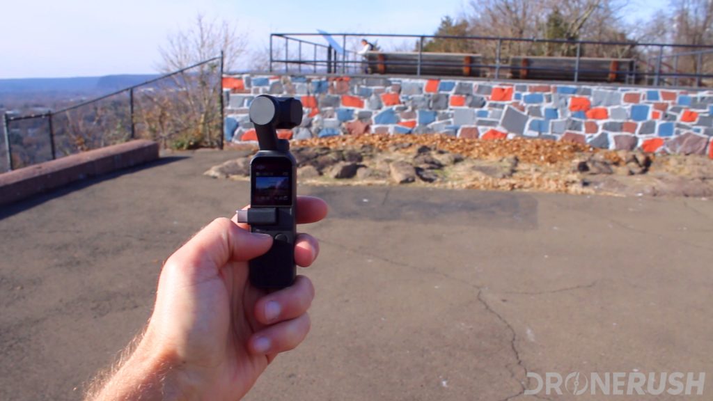 The DJI Osmo Pocket in a man's left hand held up outside to photograph a colorful wall.