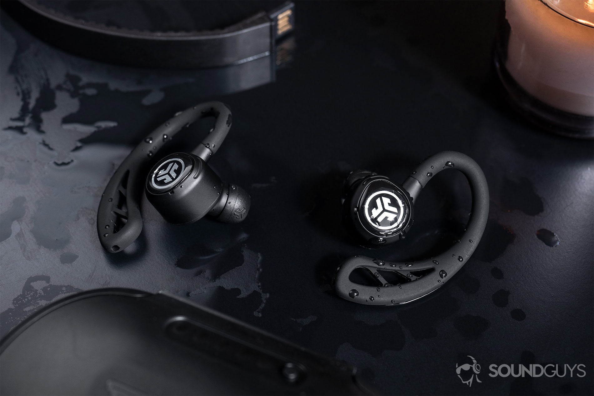 JLab  Epic Air Elite: The earbuds surrounded by water on a black table.