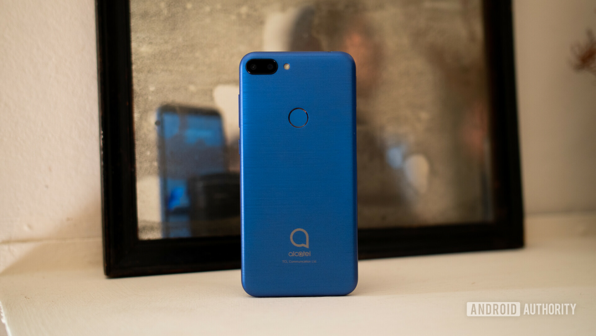 Backside photo of a blue Alcatel 1s in front of a picture frame.