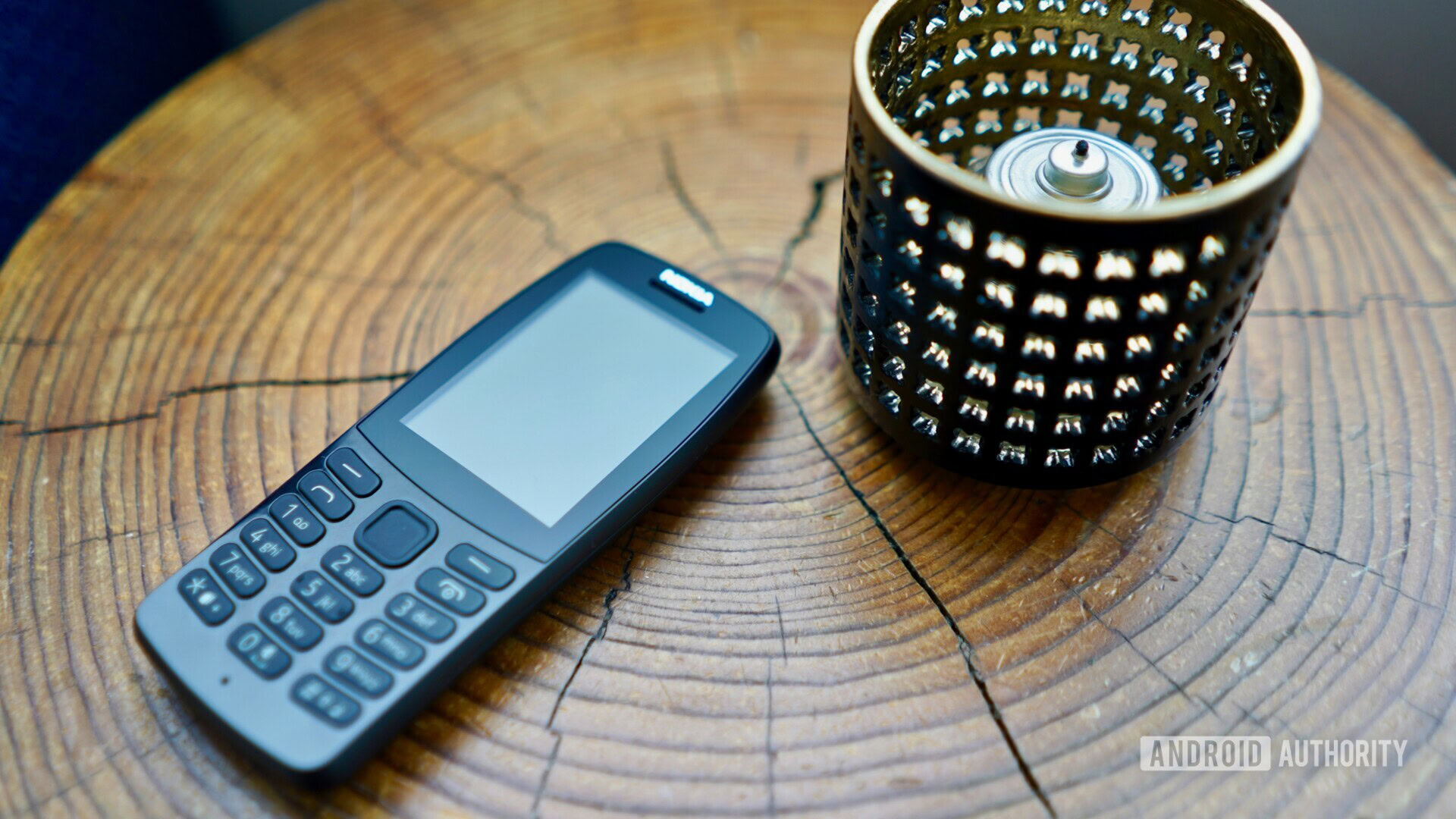 Frontside photo of the Nokia 210 laying on a tree log next to a candle.