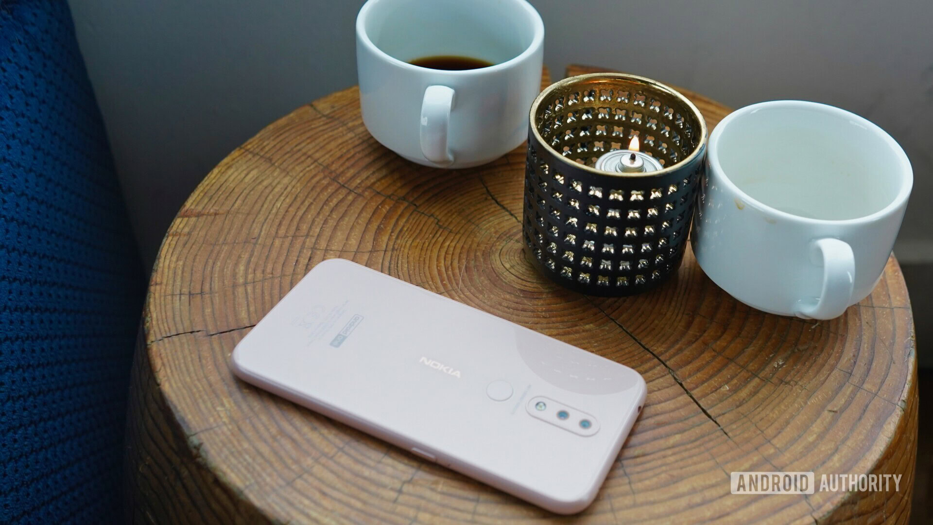 Backside photo of a white Nokia 4.2 next to couple of coffee mugs and a candle.