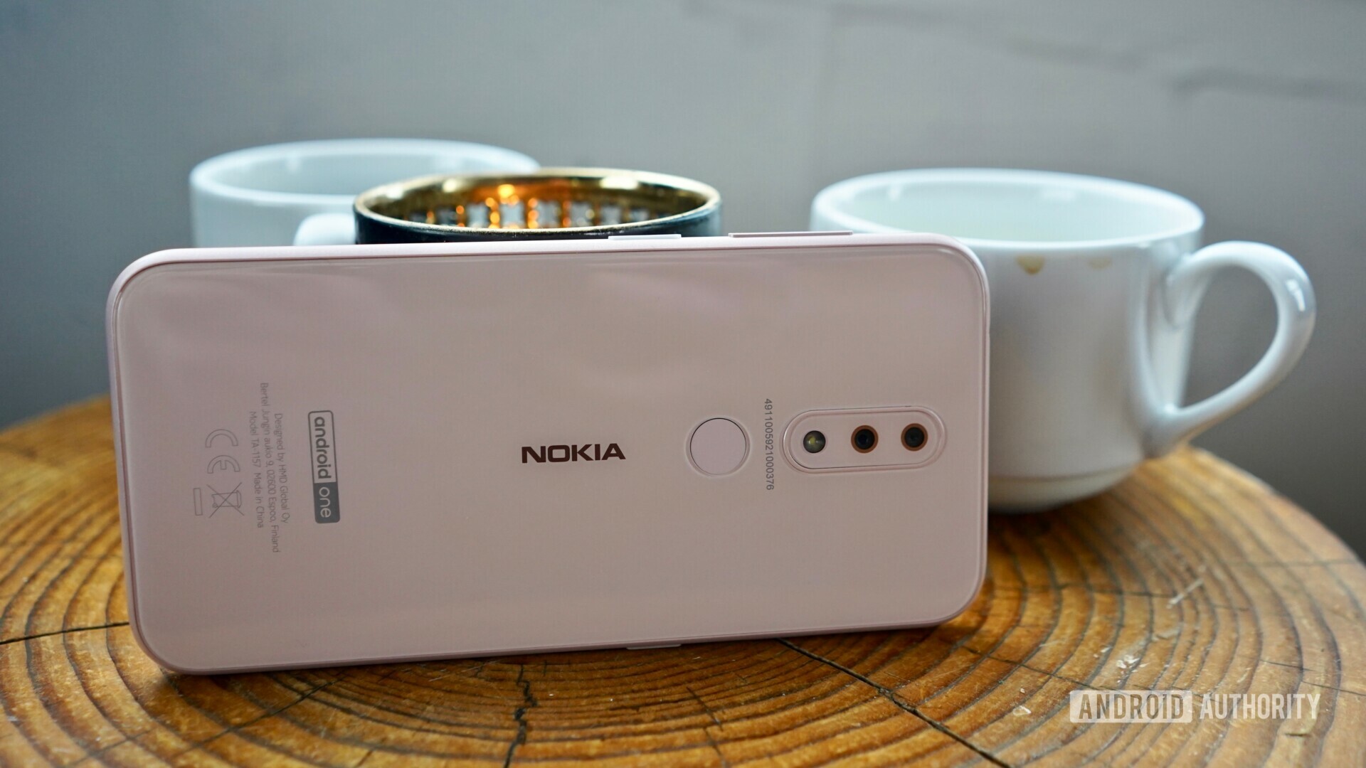 Backside photo of a white Nokia 3.2 laying horizontally in front of coffee mugs.