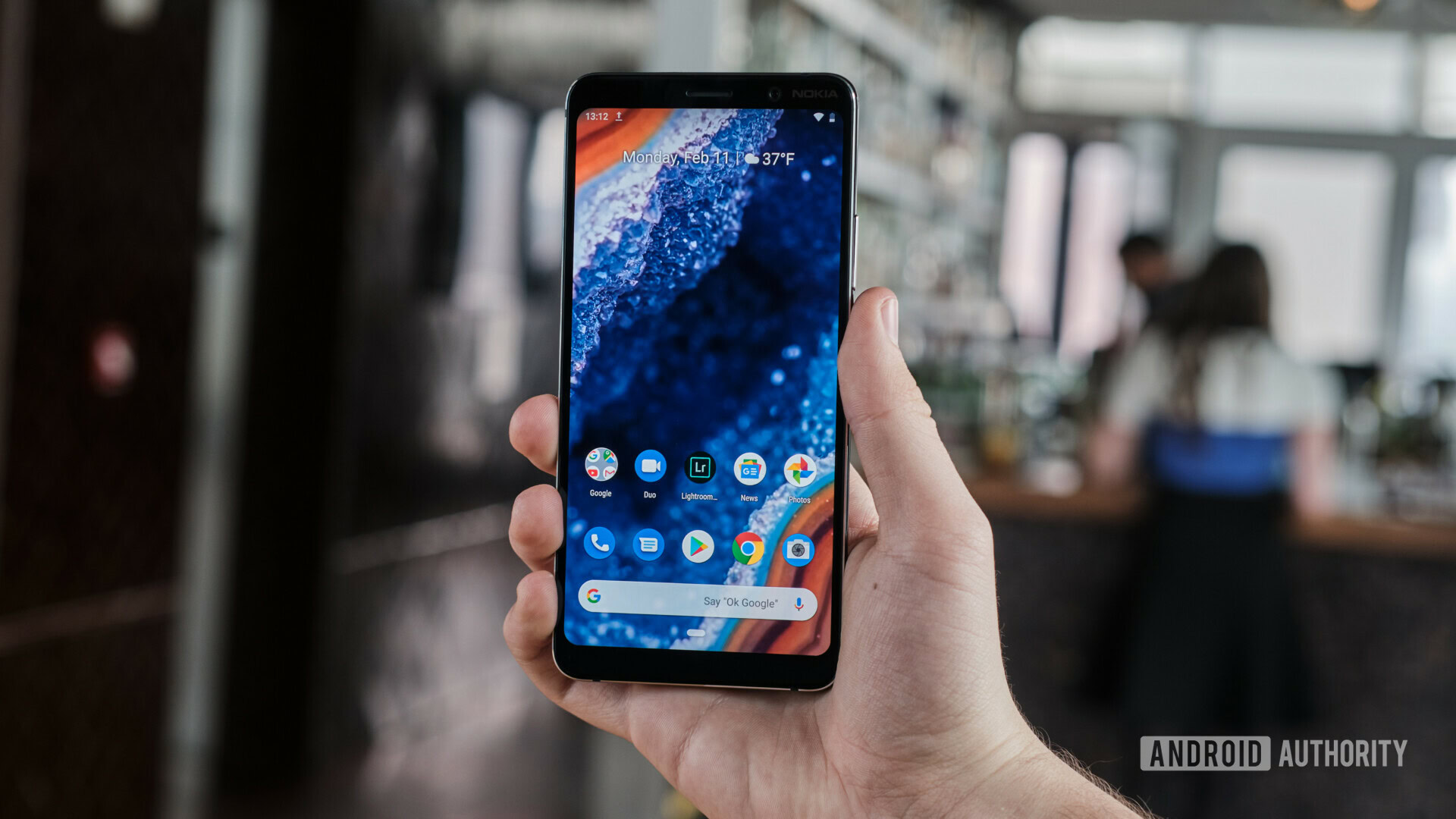 Frontside of the Nokia 9 PureView held in hand, with the display turned on and showing the default homescreen.