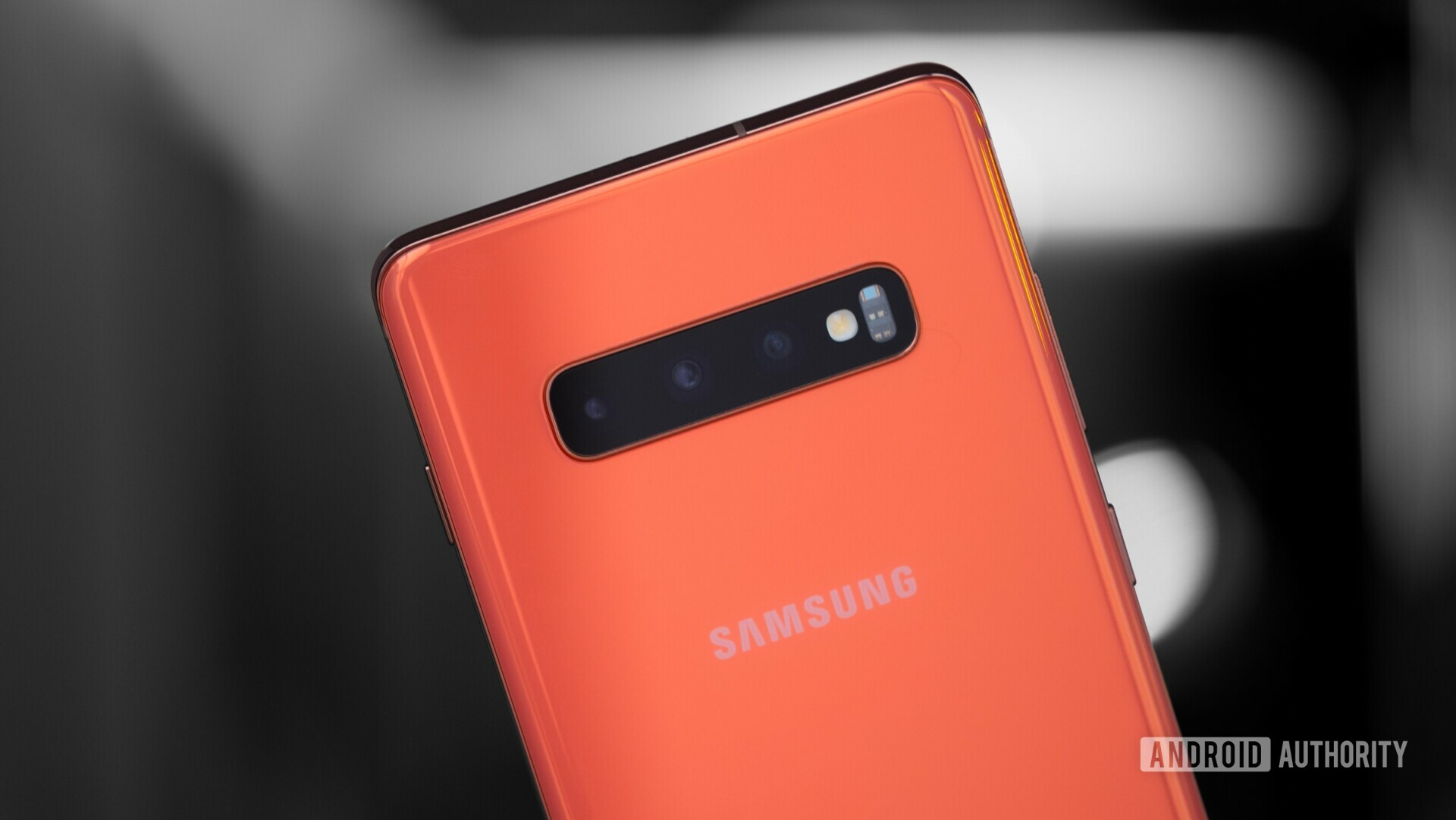 Photo of the back side tripple cameras on an orange Samsung Galaxy S10 Plus