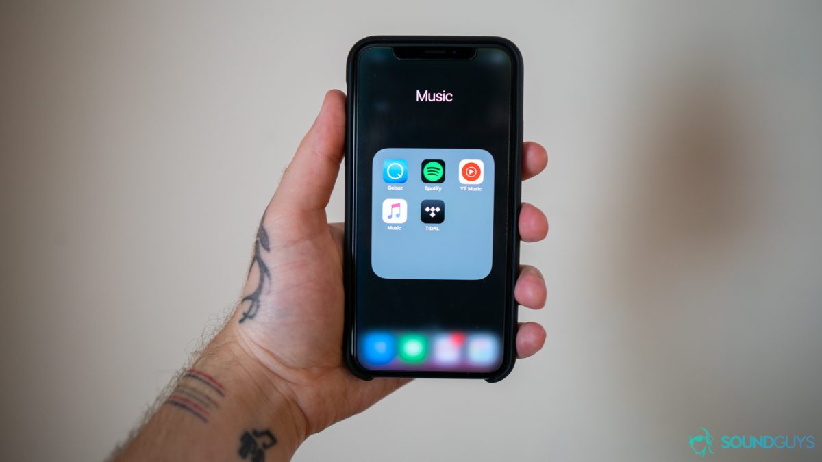 TIDAL Man holding iPhone with folder open containing various music streaming apps.