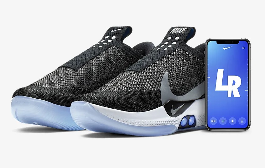 The Nike Adapt BB sneakers with a phone beside them.