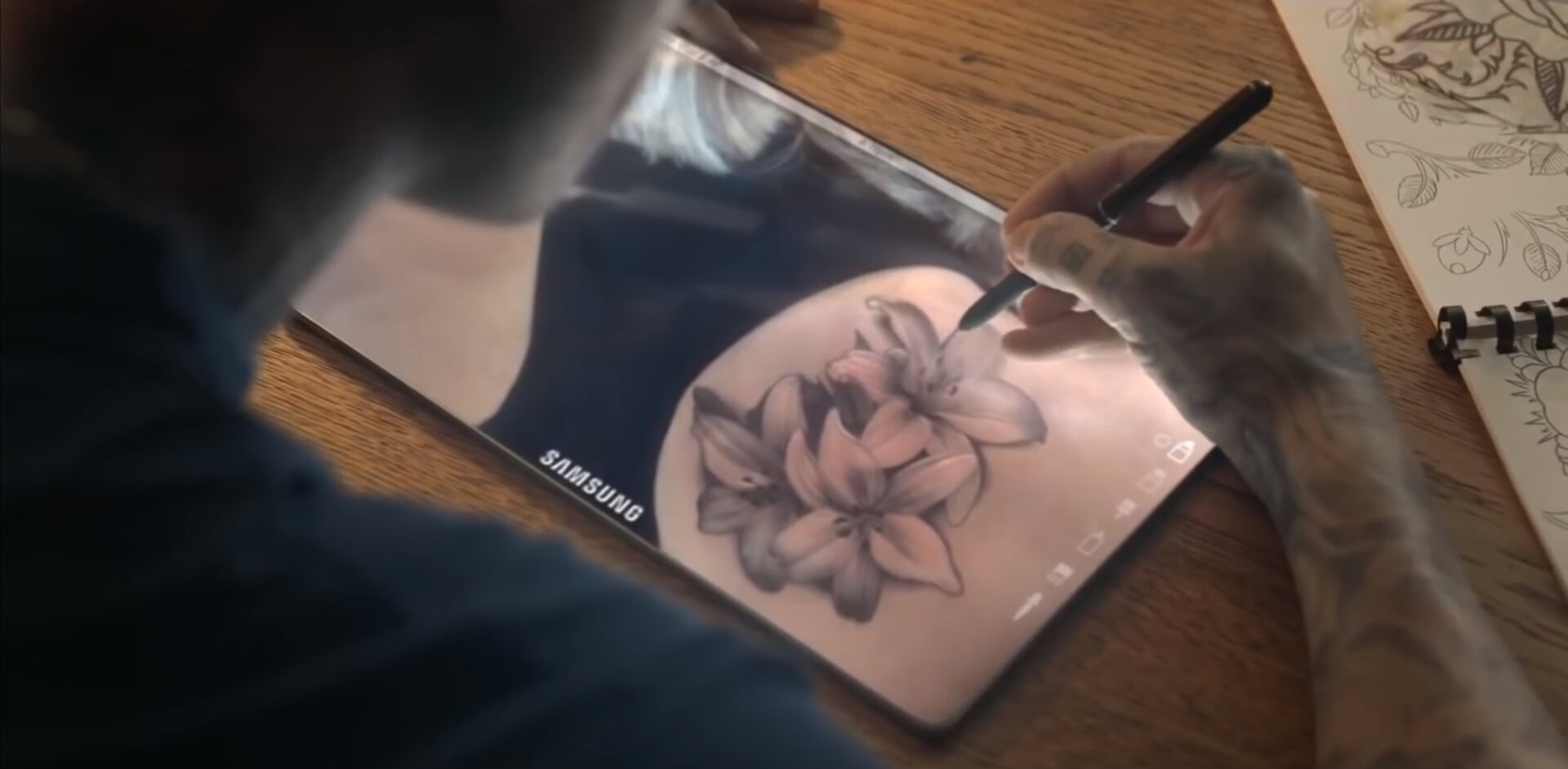 A tattoo artist drawing on a bezel-less tablet