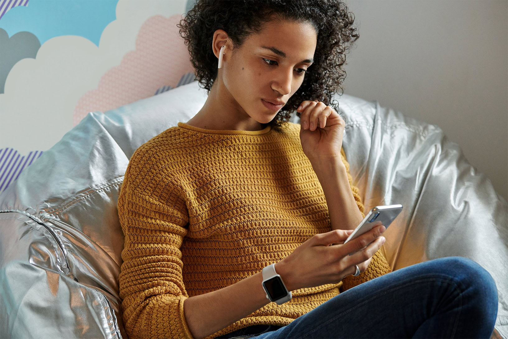 Lifestyle image of a woman wearing the second-generation AirPods on a bean bag chair.