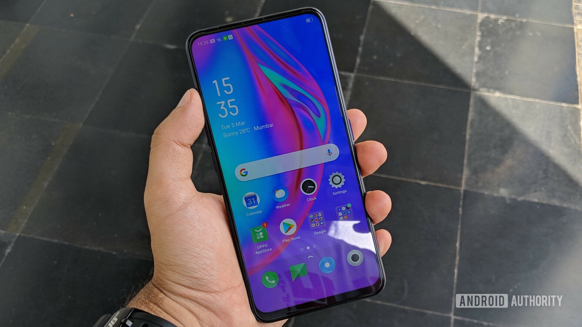 Front side of the OPPO F11 Pro held in a hand with the display turned on showing the default homescreen.