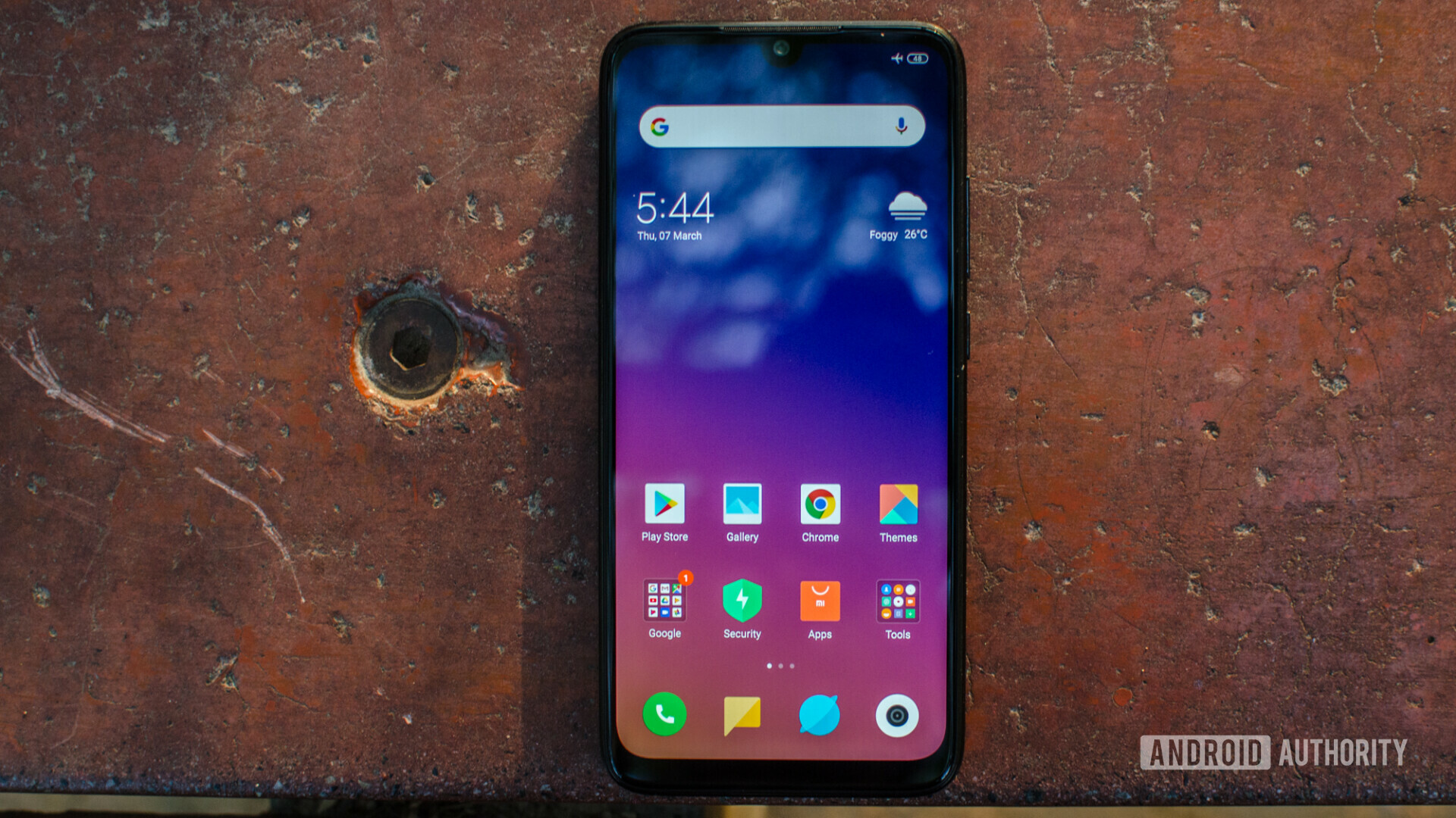 Frontside of the Redmi Note 7 Pro with the display turned on, laying on a floor.