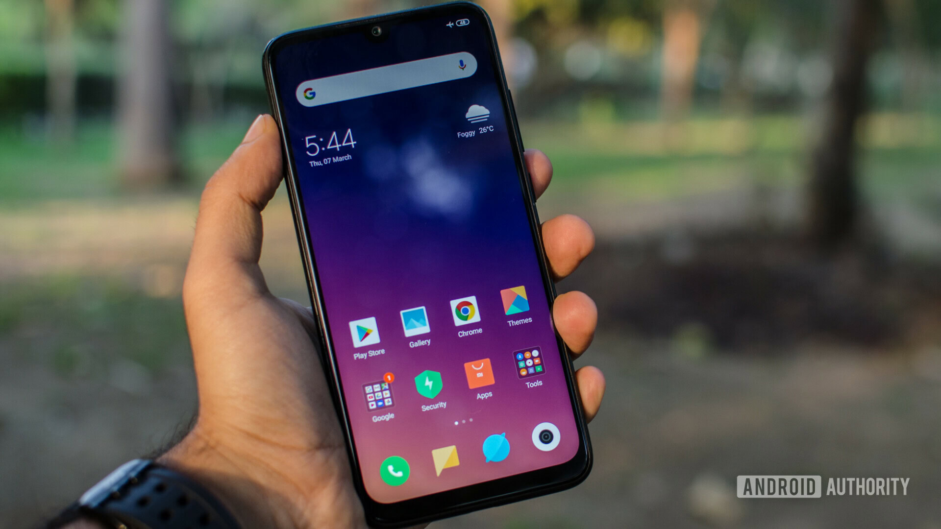 Front side of the Redmi Note 7 Pro held in hand, showing the default homescreen.