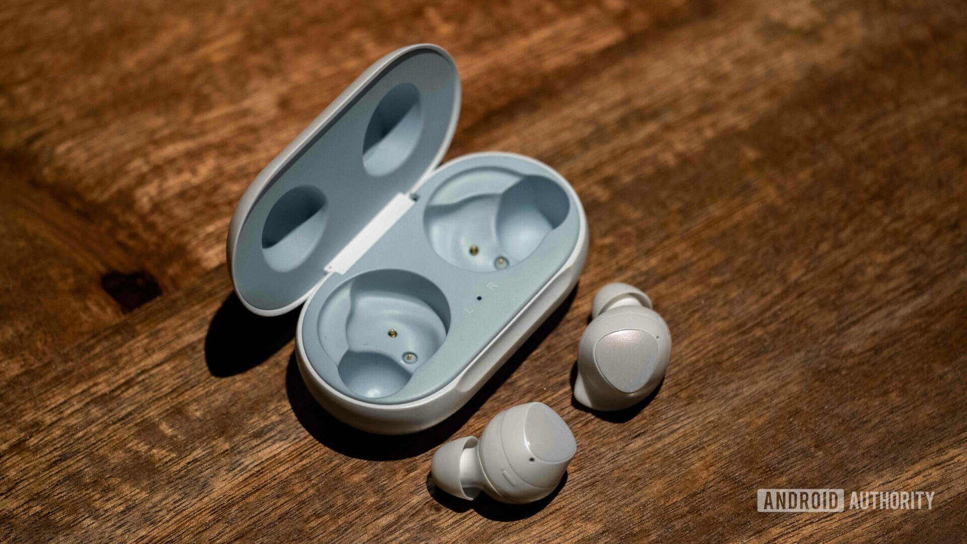 Samsung Galaxy Buds layed out on a wooden desk next to an opened case.