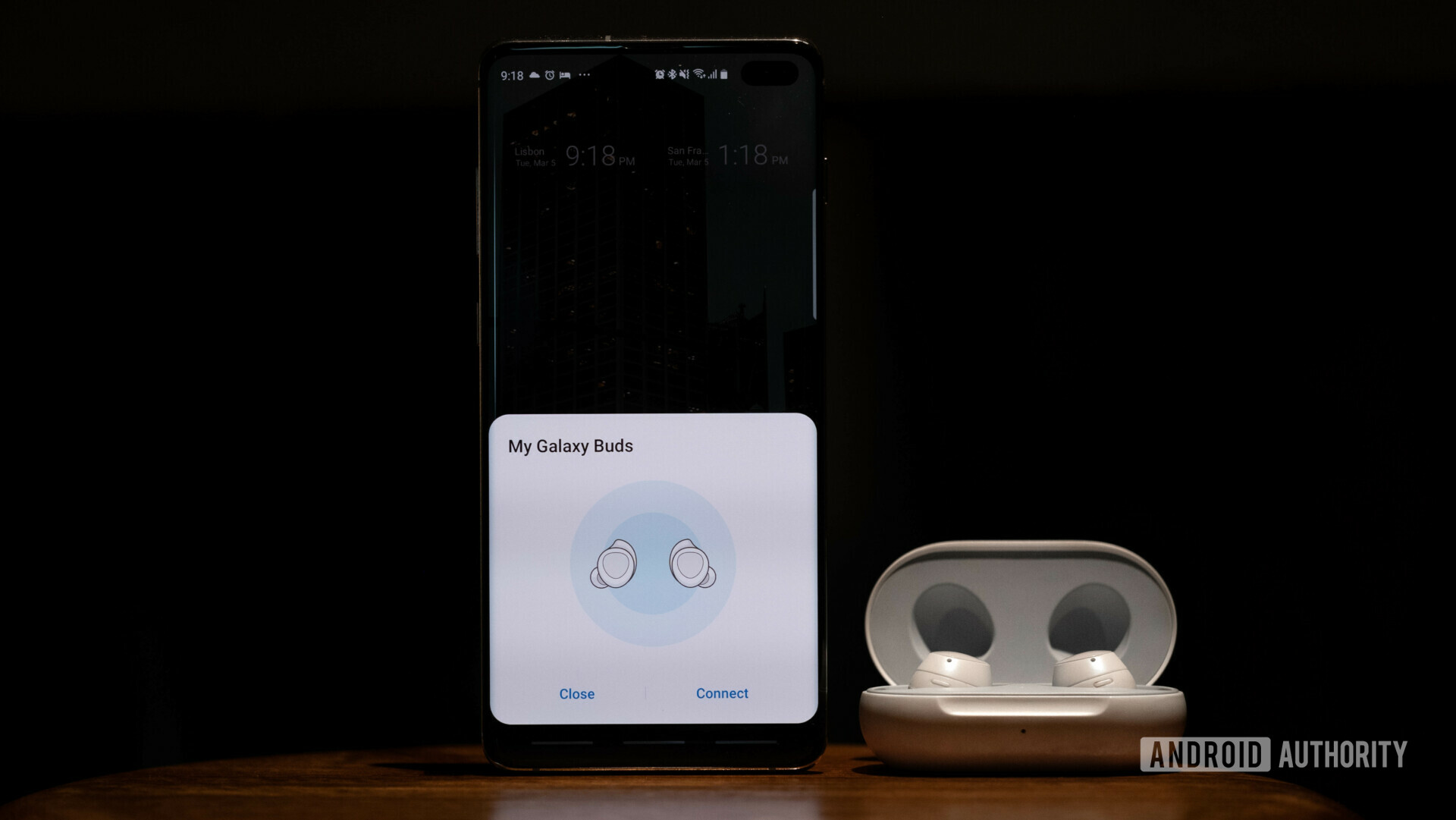 Samsung Galaxy Buds in a case next to a Galaxy S10 showing the pairing menu.