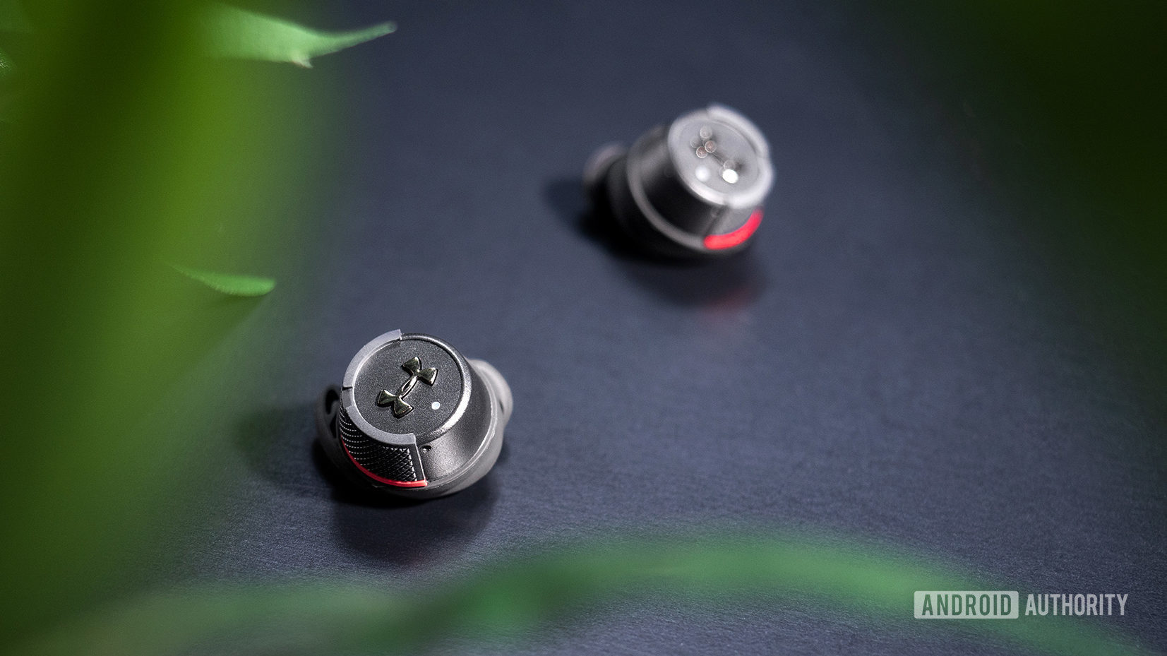 Under Armour True Wireless Flash JBL: Solo image of the earbuds on a black table.