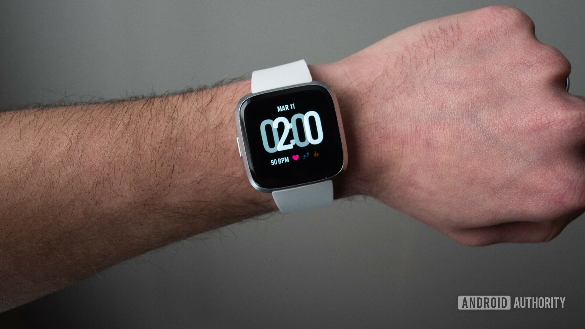 Fitbit Versa Lite with a white band worn on a wrist.