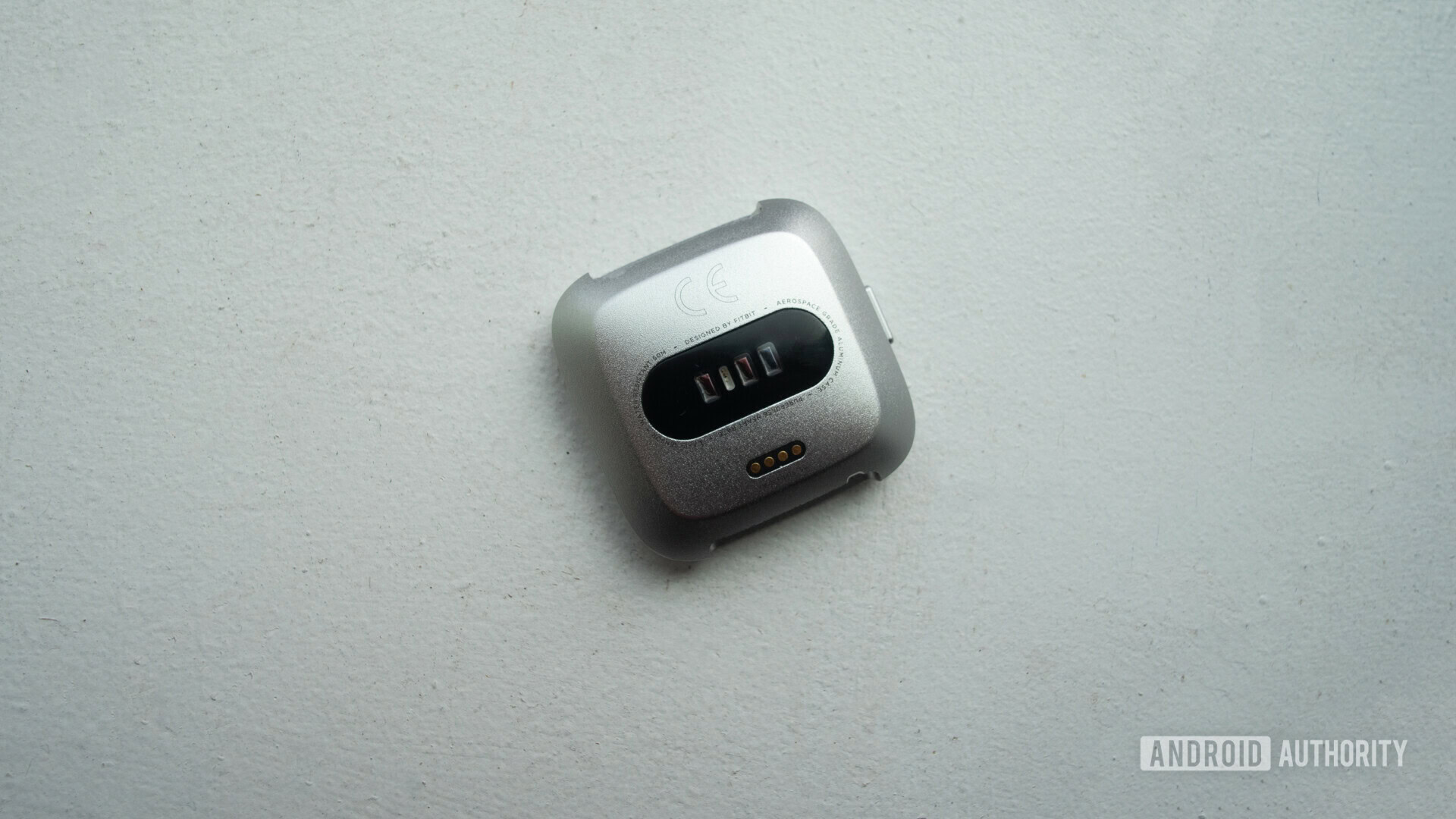 Backside of the Fitbit Versa Lite showing the heart rate monitor sensor and charging pins.