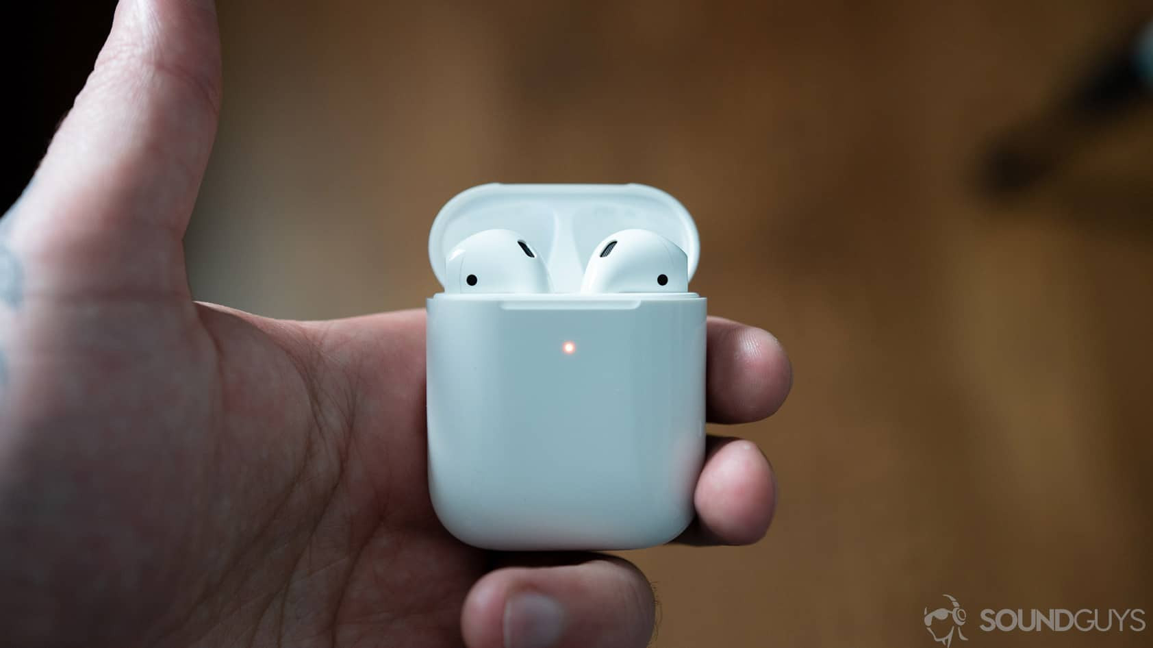 The Apple AirPods in wireless charging case held by man's hand.