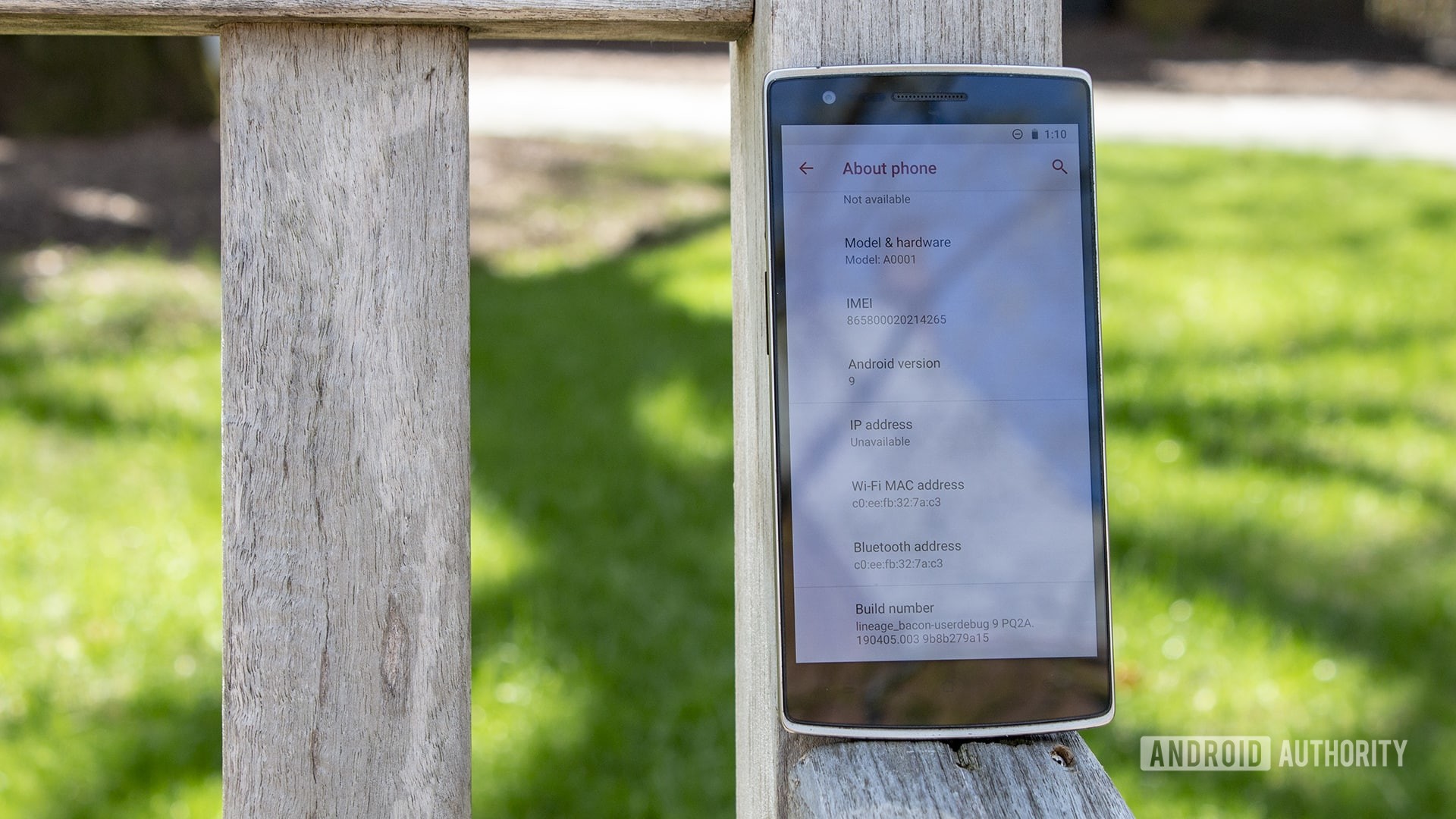 A OnePlus One leaning on a bench with the About Phone page pulled up.