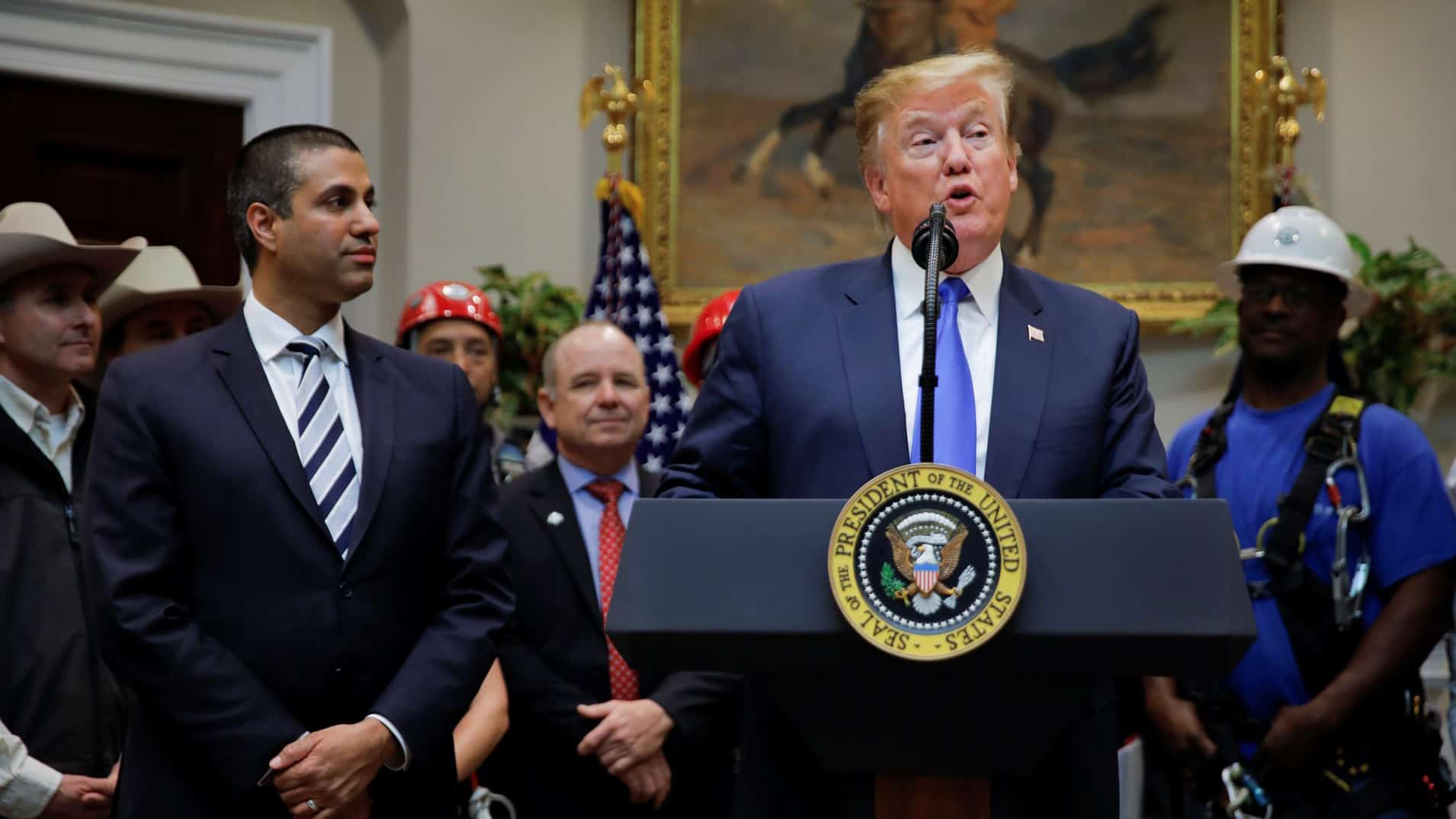 President Donald Trump standing at a press podium next to FCC chairman Ajit Pai as Trump delivers a speech about 5G plans for the United States.