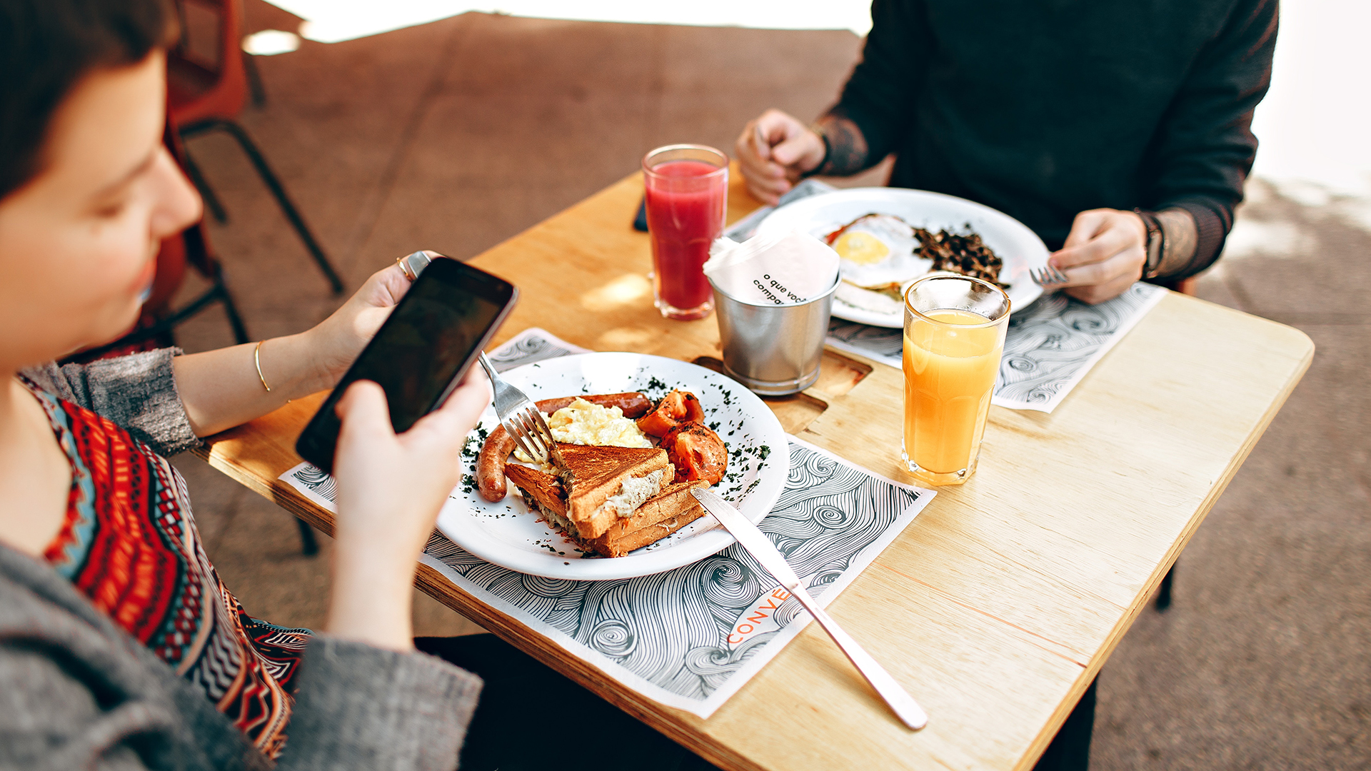 An image of two people dining out with one using Google Maps on their smartphone to photograph a popular dish.