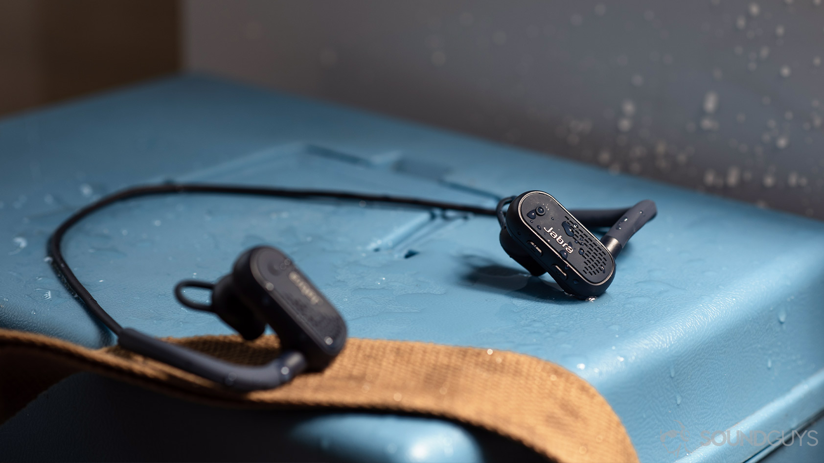 A picture of the Jabra Elite Active 45e neckband workout earbuds covered in water on a blue surface.