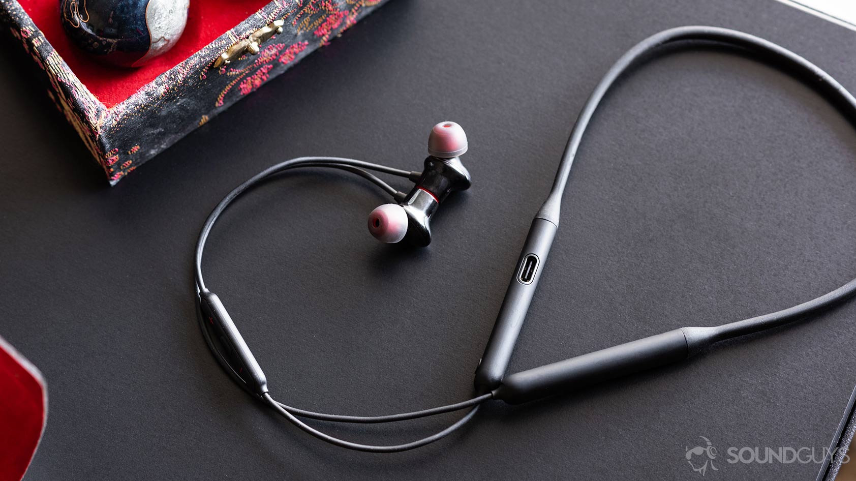 A picture of the OnePlus Bullets Wireless 2 earbuds and neckband with the cable curling up and around on a black table.