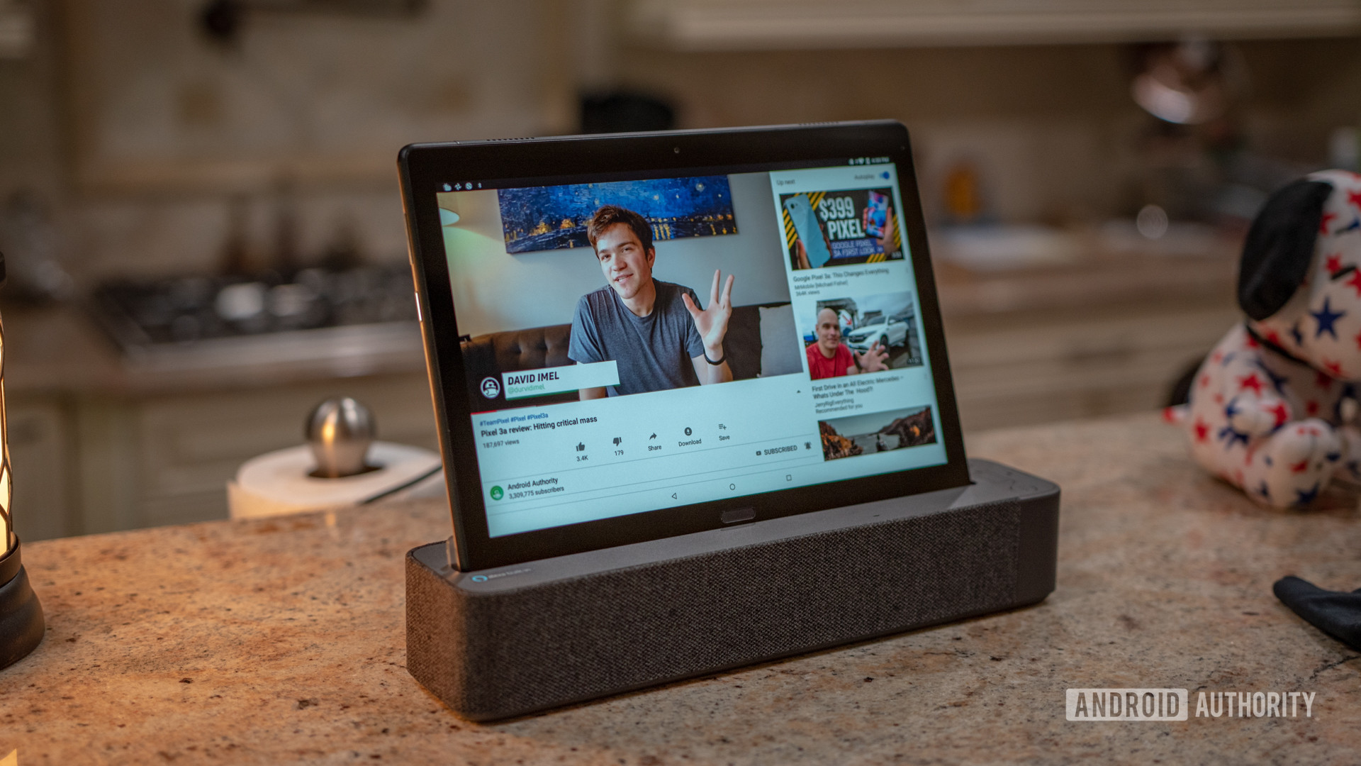 A Lenovo Smart Tab P10 in its dock on a kitchen counter showing a YouTube video