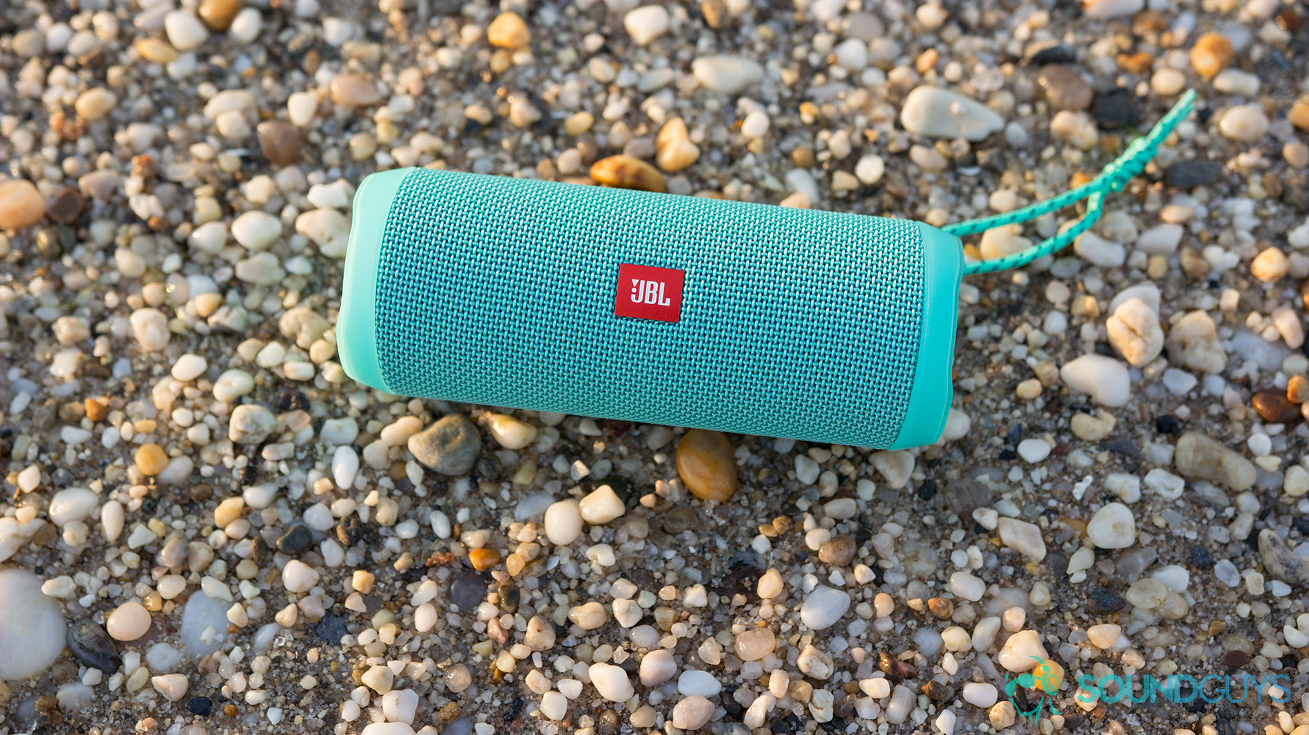 The JBL Flip 4 Bluetooth speaker on a rocky beach.