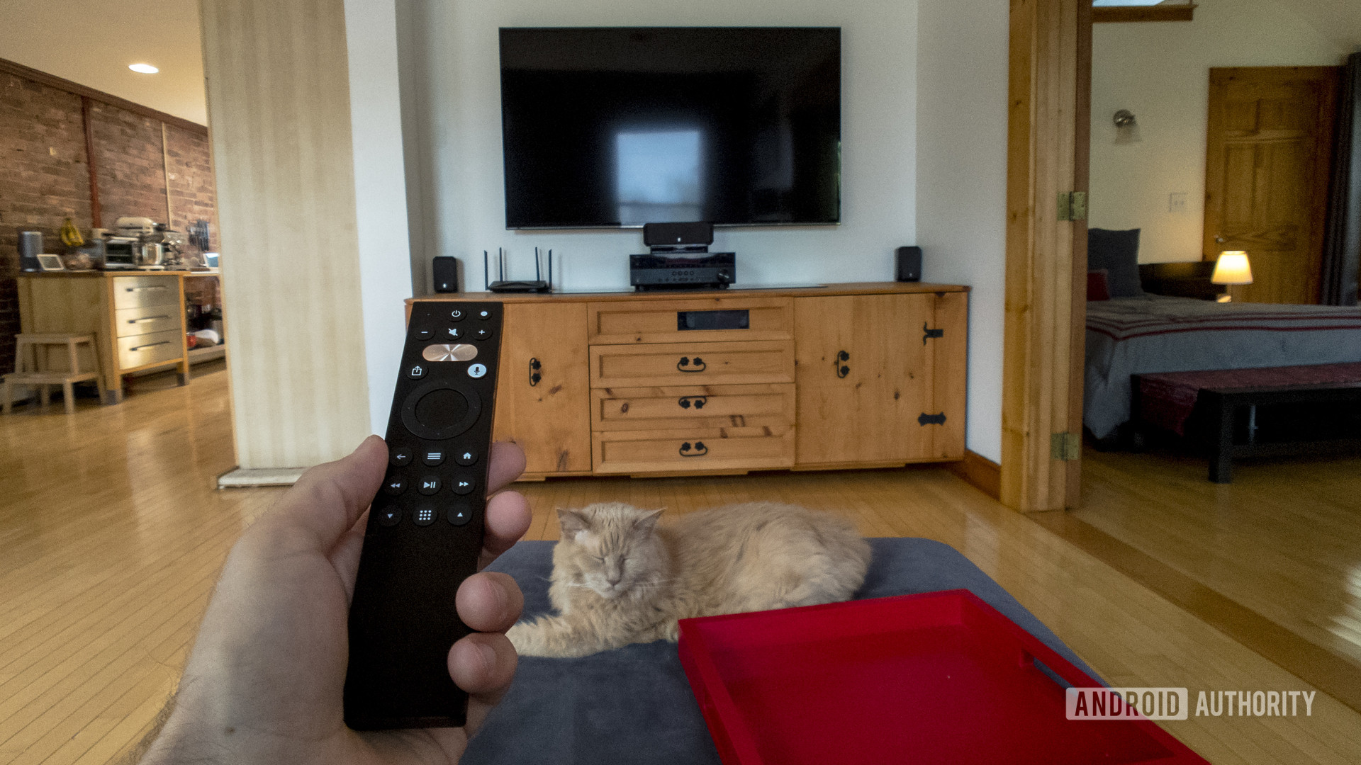 A first-person view of a man sitting on a couch with a Caavo Universal Remote in his hand.